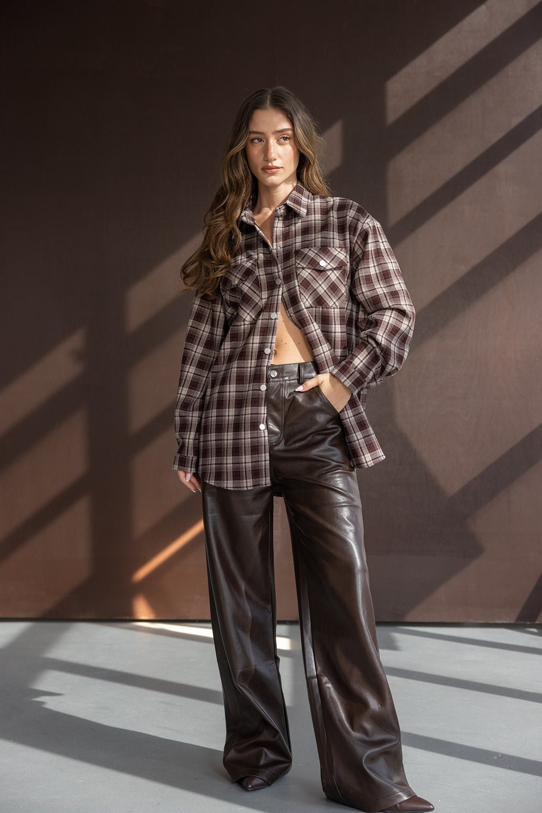 אישה עם חולצת פלאנל משובצת חומה ומכנסי עור רחבים חומים, אופנת חורף לנשים