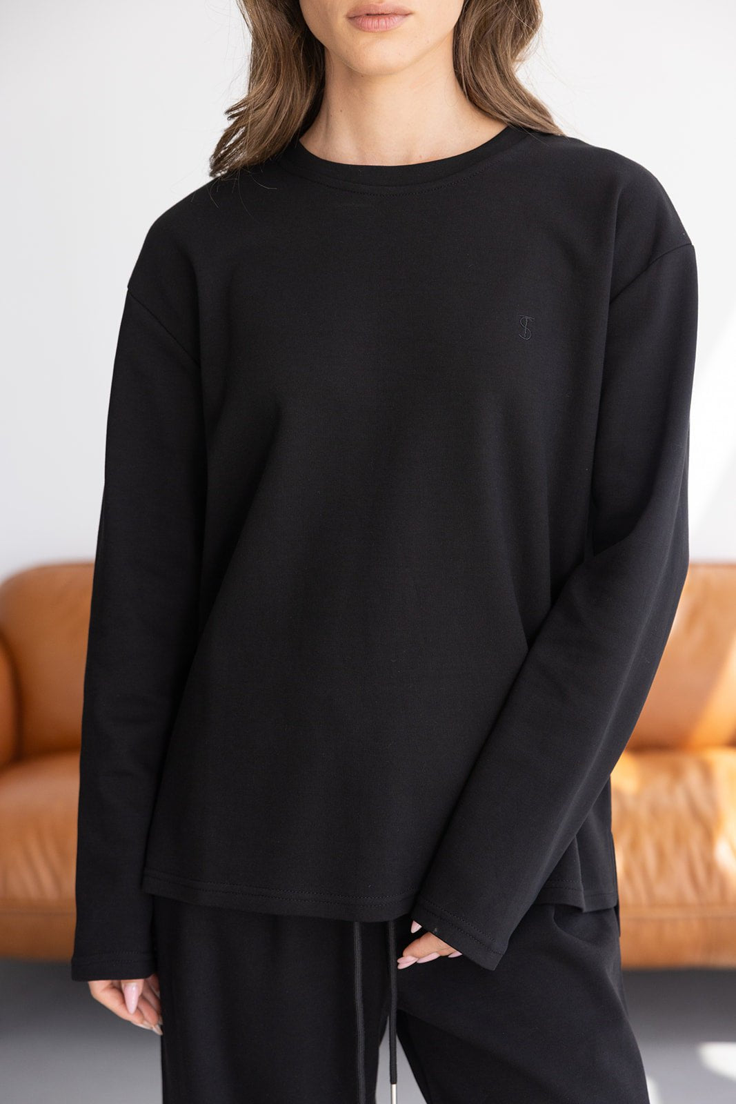 אישה לובשת חולצת טרנינג שחורה ארוכה לנשים, בסגנון קז'ואל, רקע ביתי ובסיסי