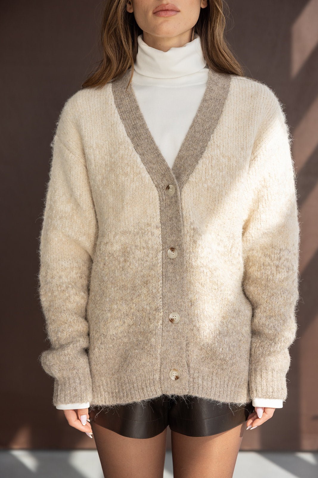 קרדיגן נשים סרוג בגווני בז' עם כפתורים, מעל גולף לבן ומכנסיים קצרים שחורים, אופנת חורף