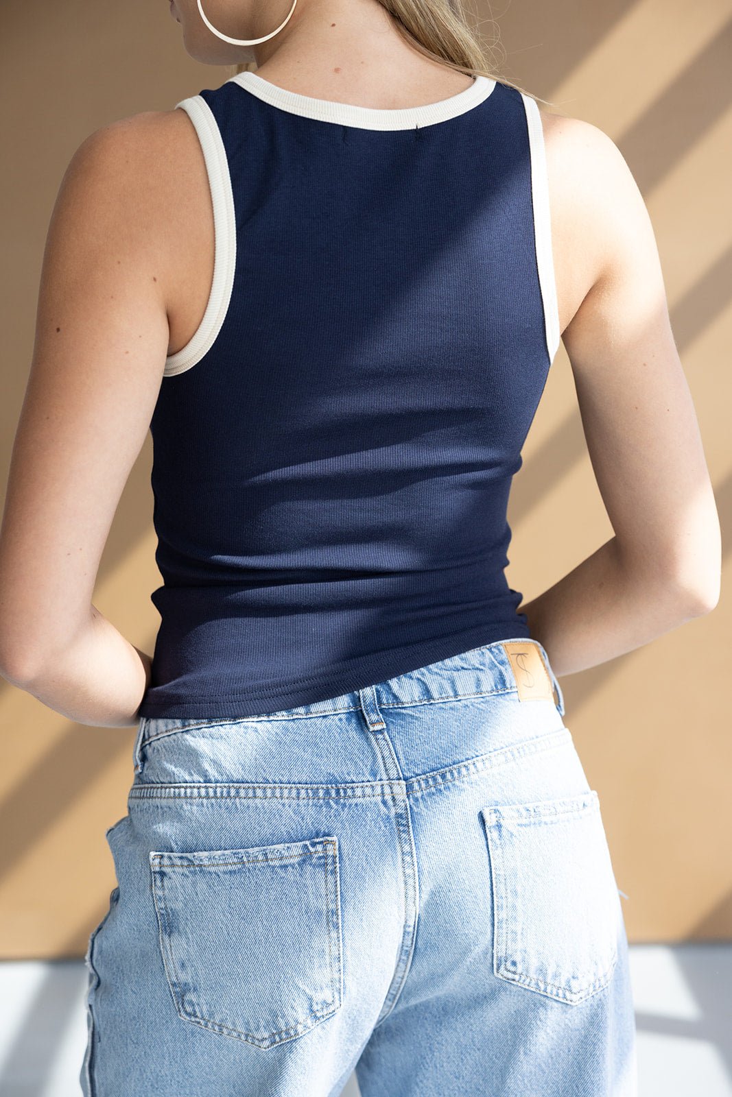 אישה עם גופיה כחולה בגזרה ספורטיבית ומכנסי ג׳ינס גבוהים, אופנת נשים קז'ואל