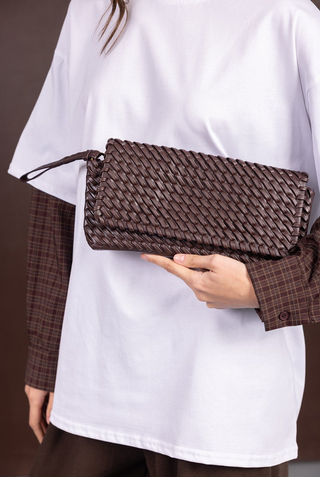 אישה מחזיקה תיק קלאץ' קלוע חום, חולצה לבנה עם שרוולים משובצים, אופנה לנשים