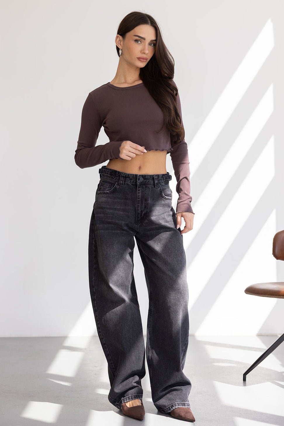 אישה לובשת חולצת קרופ ארוכה בצבע חום כהה עם ג'ינס שחור רחב, אופנת נשים עדכנית