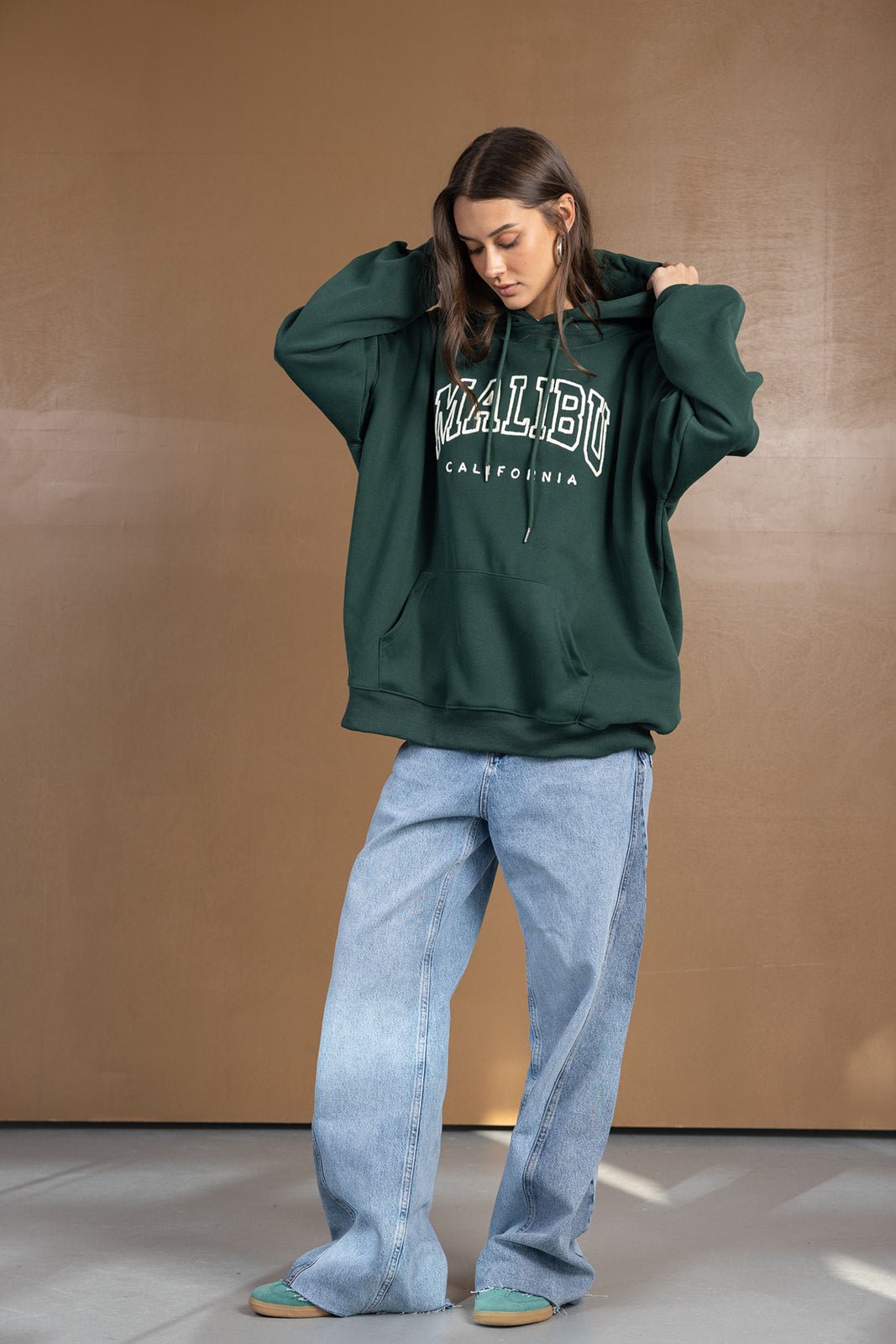 דוגמנית לובשת קפוצ'ון ירוק עם כיתוב MALIBU ומכנסי ג'ינס רחבים, ביגוד אופנתי לנשים