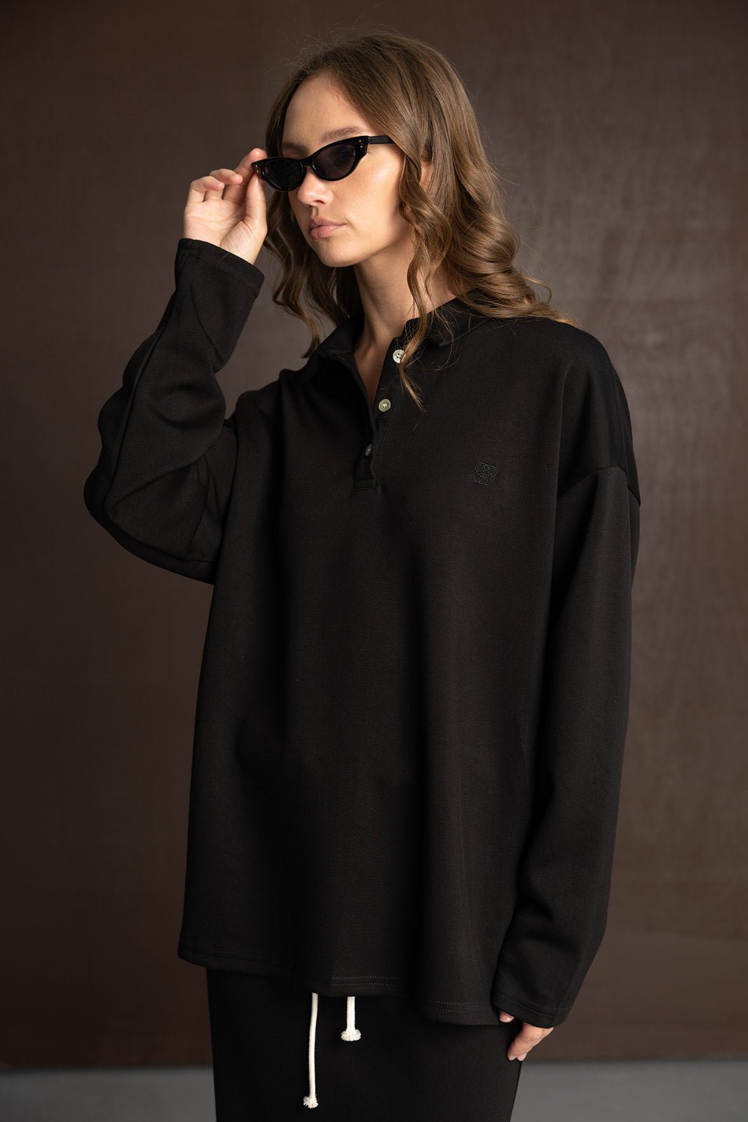 אישה עם חולצת פולו שחורה ארוכה ואופנתית, לובשת משקפי שמש, סטייל טרנדי לנשים