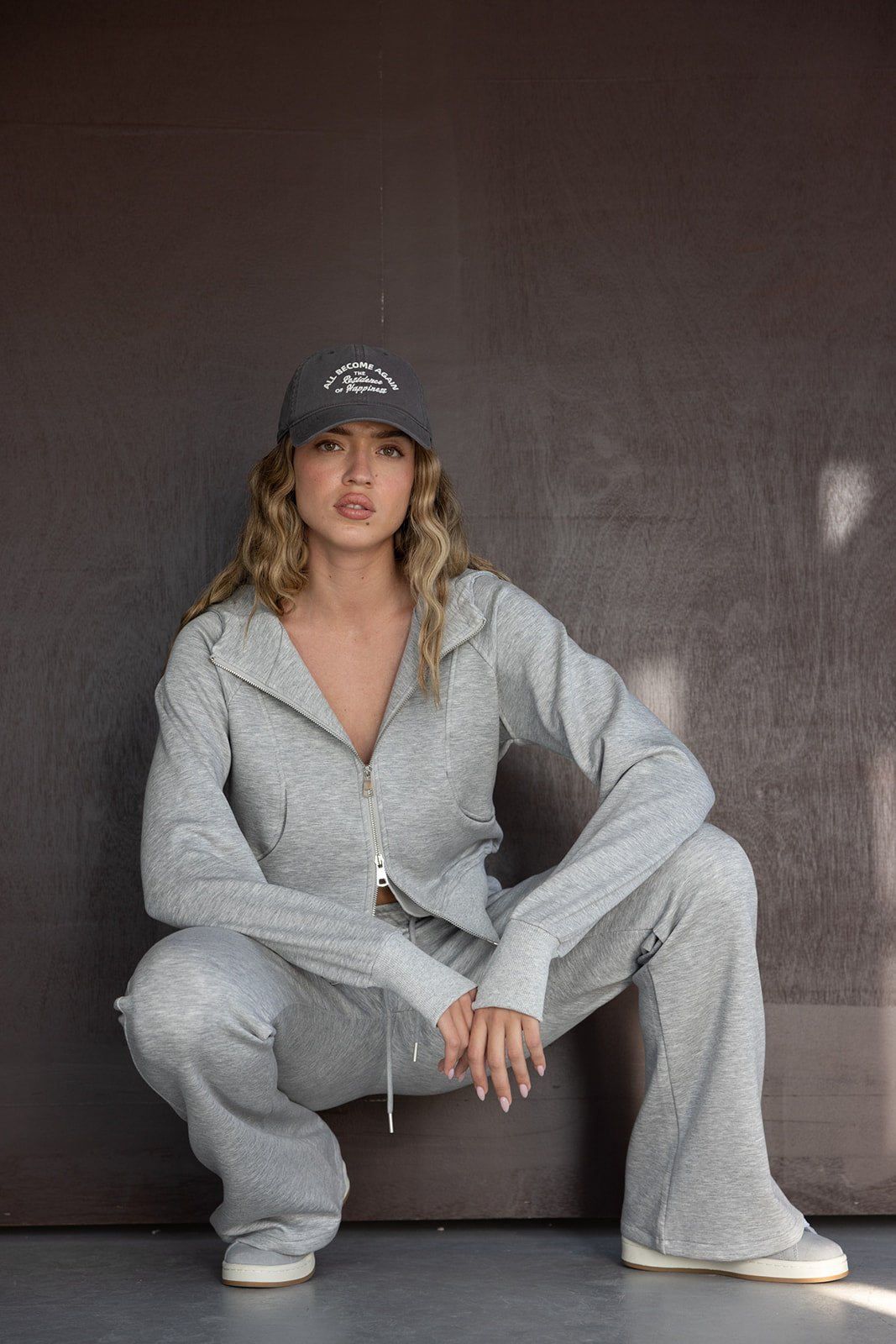 דוגמנית יושבת בטרנינג אפור וכובע מצחייה, אופנת נשים קז'ואל