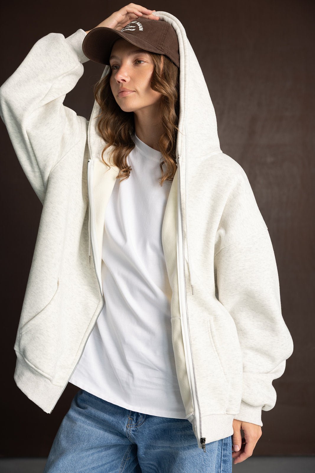 אישה עם קפוצ׳ון בז׳ פתוח, טי שרט לבנה, ג׳ינס וכובע מצחיה חום, לוק אופנתי יומיומי לנשים