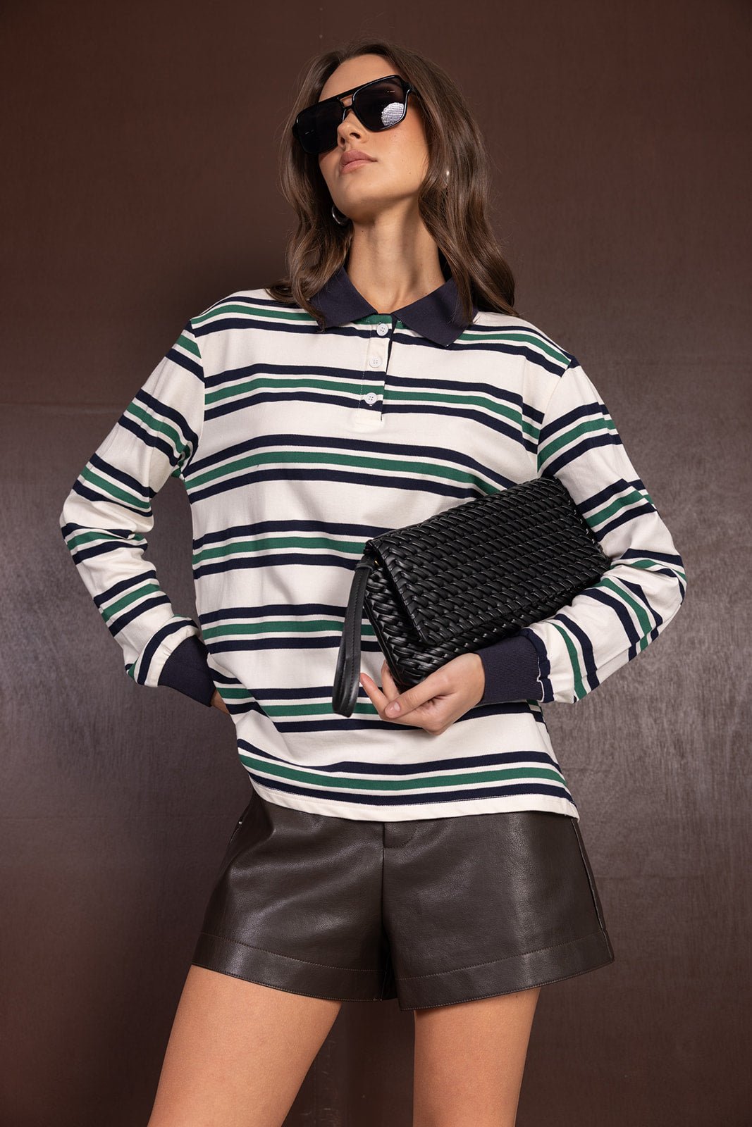 אופנת נשים: דוגמנית עם חולצת פסים ארוכה, שורט עור שחור, משקפי שמש ותיק קלאץ' קלוע
