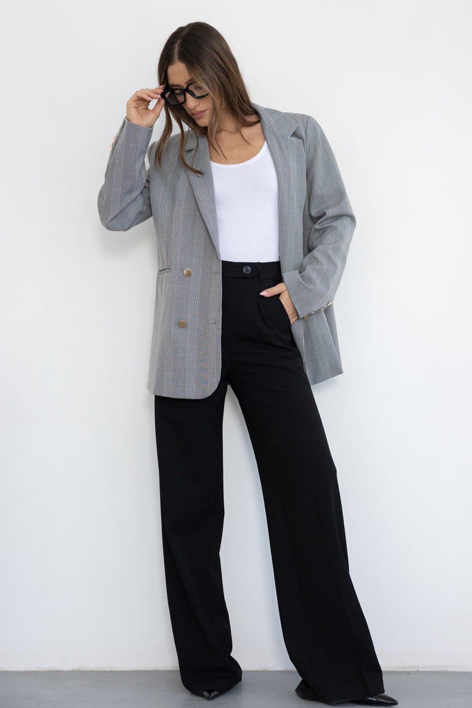 אישה עם ז'קט אפור מחויט, חולצה לבנה ומכנסיים שחורים רחבים, לוק אופנתי לנשים