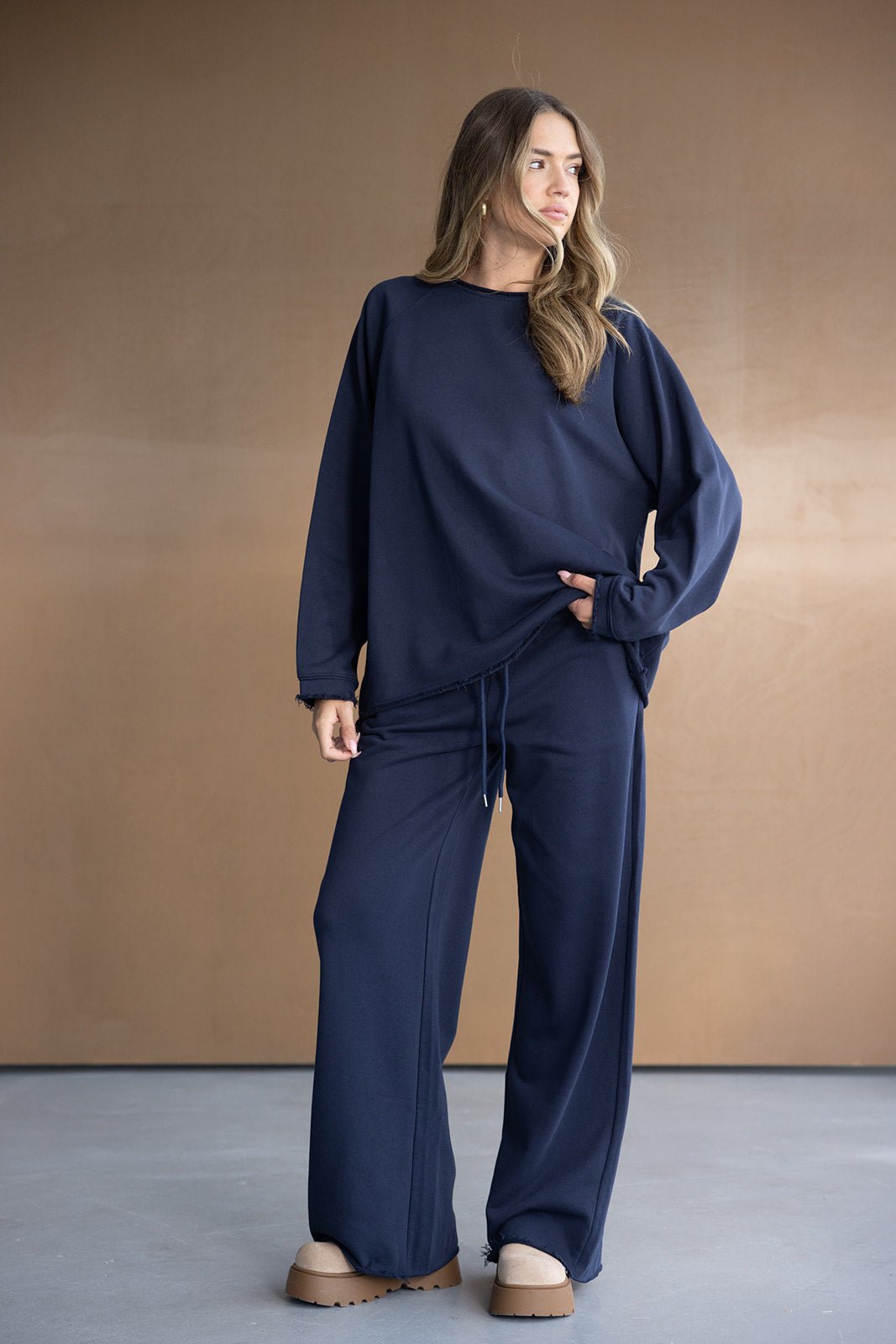 אישה לובשת חליפת טרנינג כחולה אופנתית, חולצה ארוכה ומכנסיים רחבים, נעלי פלטפורמה בז'.