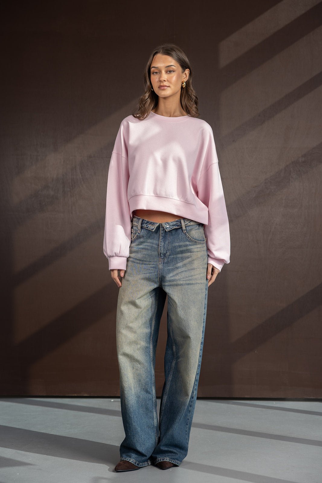 דוגמנית לובשת סווטשירט ורוד בגזרה רחבה עם מכנסי ג'ינס רחבות, אופנת נשים צעירה