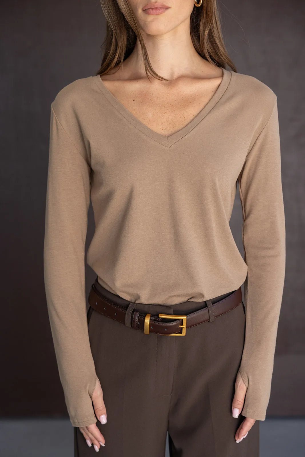 חולצת נשים בצבע בז' עם שרוולים ארוכים ומחשוף וי, משולבת במכנסיים חומים וחגורה אופנתית