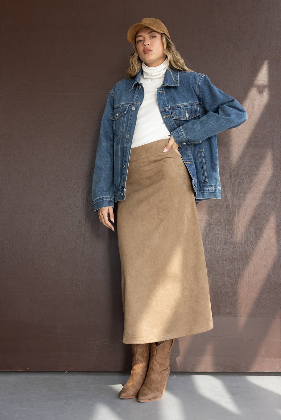 אישה צעירה לובשת ג'קט ג'ינס, חצאית מידי בצבע בז', מגפיים וחולצה לבנה, לוק אופנתי חורפי