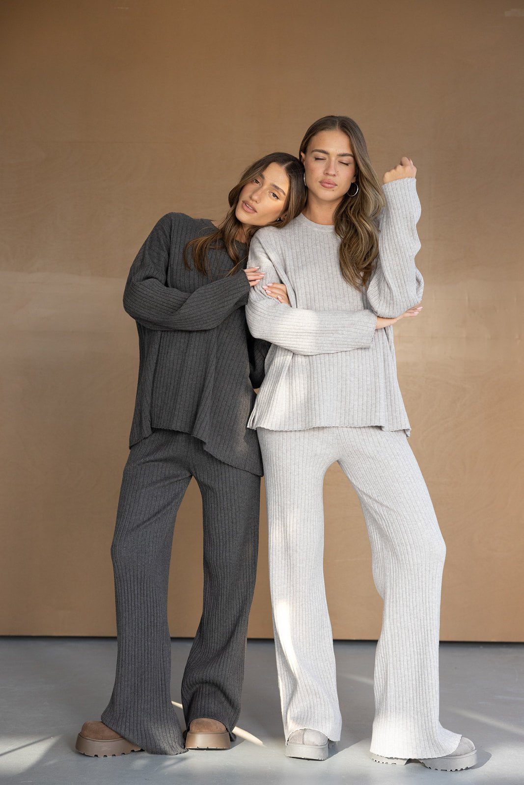 שתי נשים לובשות חליפות סריג אופנתיות בצבעים בהירים וכהים, עומדות על רקע חום