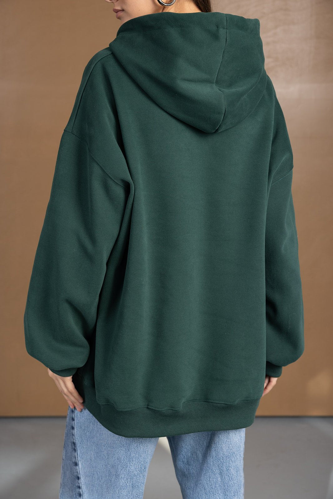 אישה לובשת קפוצ'ון ירוק אוברסייז ומכנסי ג'ינס, מצולמת מגב על רקע חום