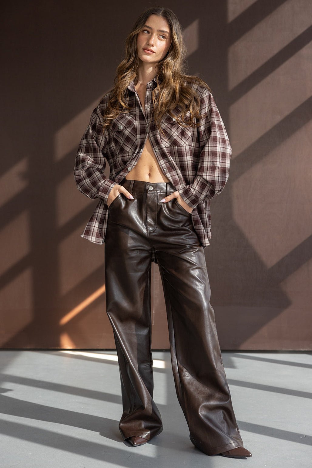 דוגמנית לובשת חולצת פלנל משובצת ומכנסי דמוי עור חומים, אופנת נשים צעירה ומודרנית