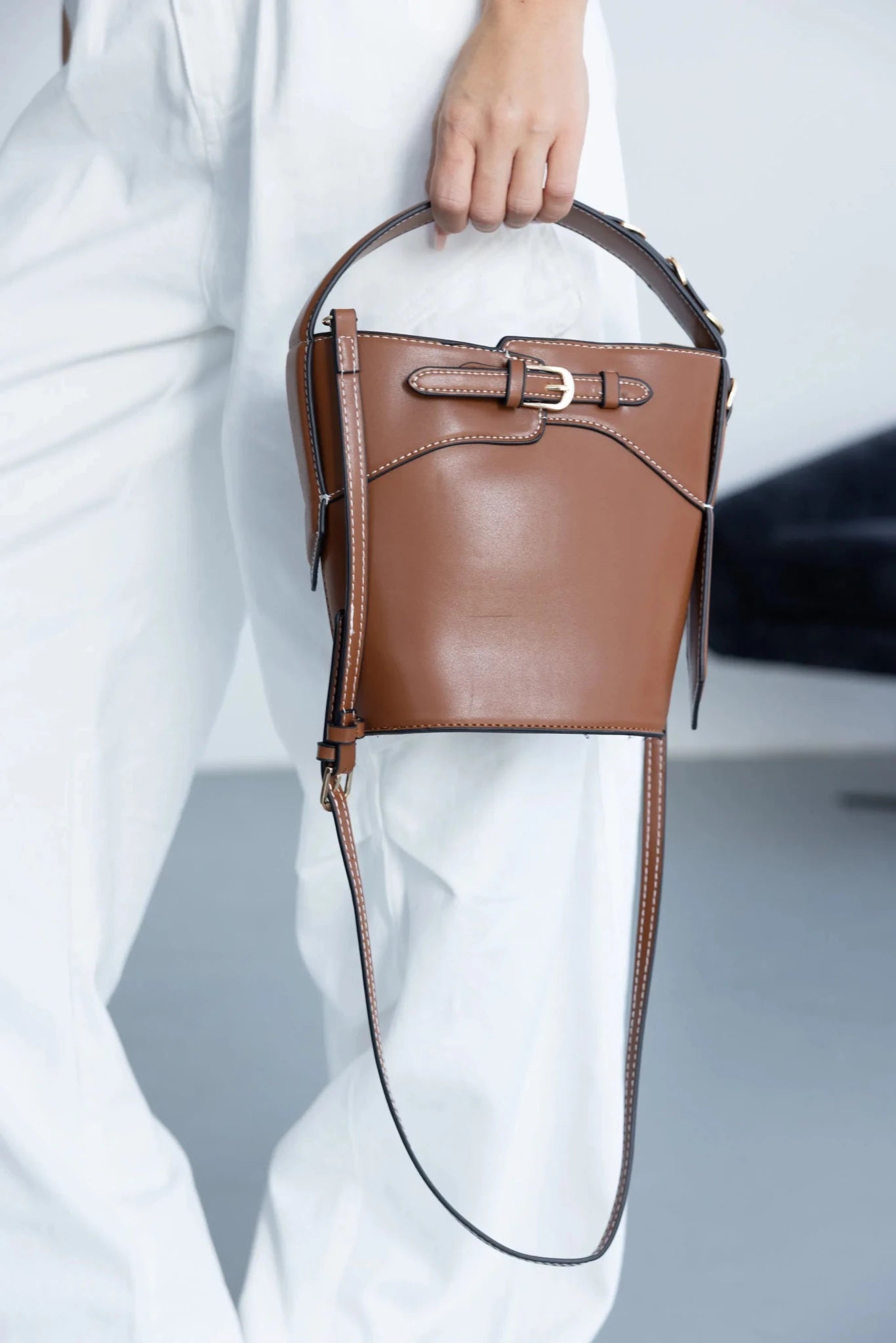 תיק צד חום לאישה עם אבזם זהב, מעוצב בקווים מודרניים, מוחזק ביד על רקע לבן