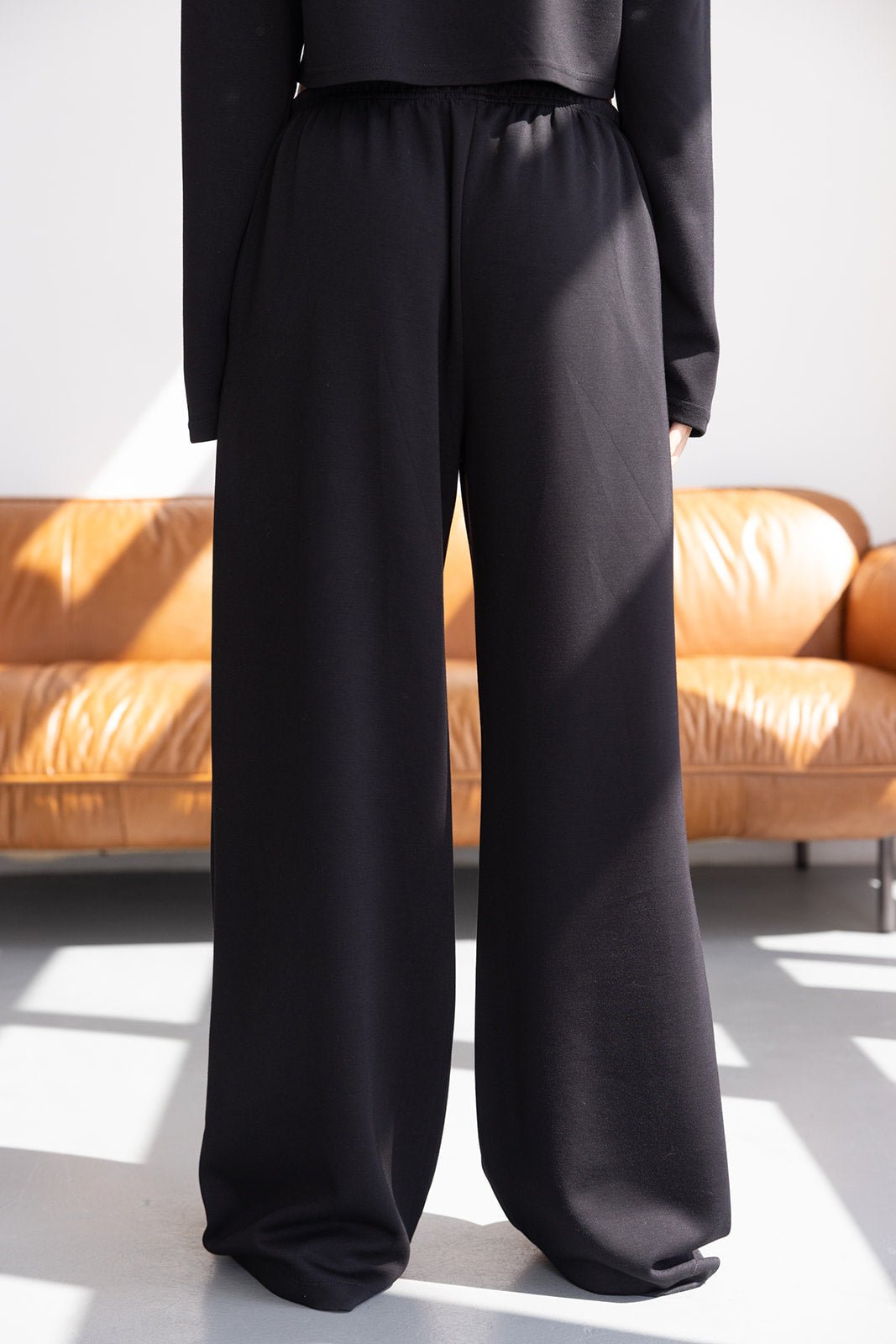 מכנסיים רחבות לנשים בצבע שחור, בד נעים ונופל, צילום באור טבעי על רקע ספה