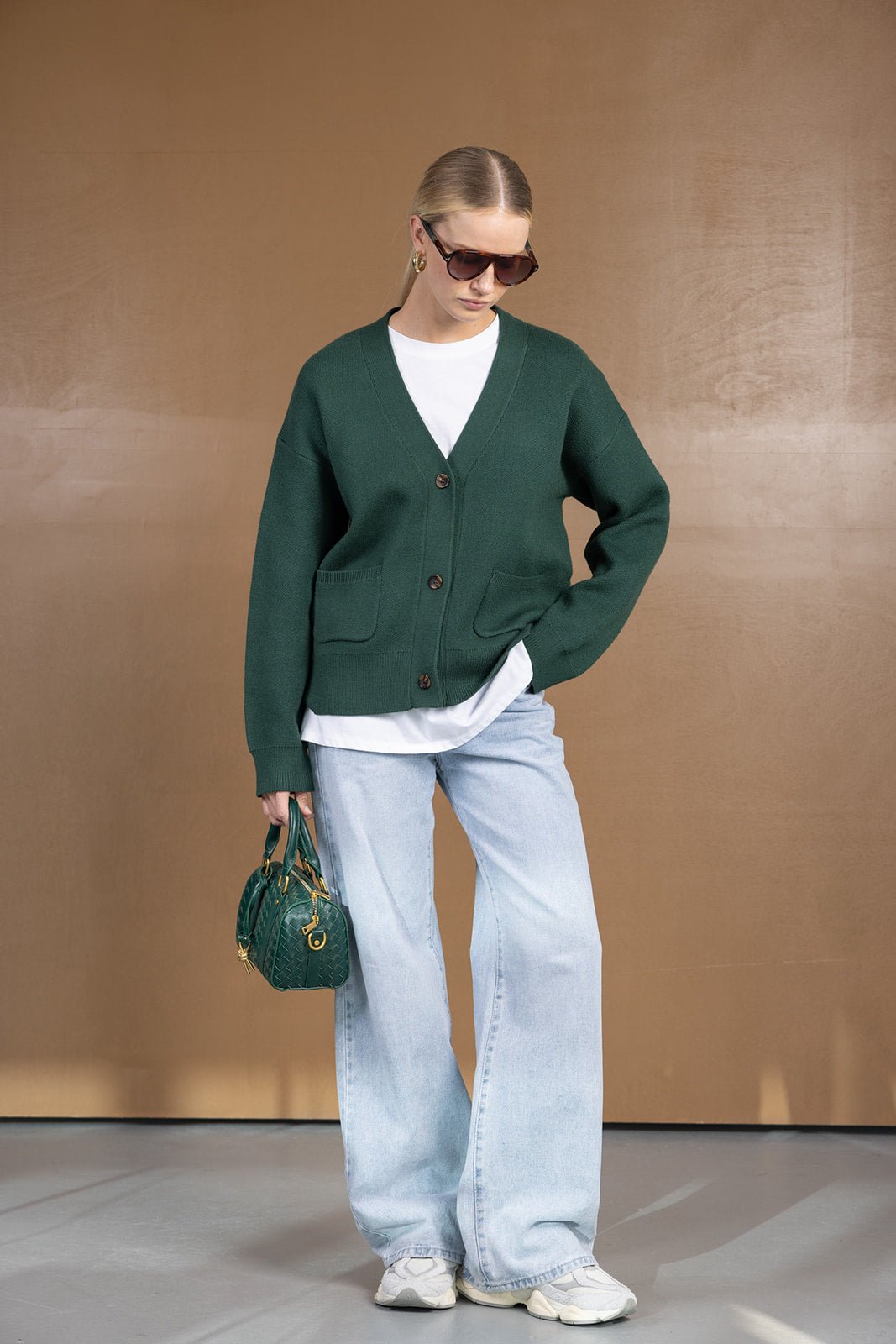 אישה עם קרדיגן ירוק, טי שרט לבנה, ג'ינס רחב תכלת, תיק ירוק ומשקפי שמש – אופנת נשים טרנדית