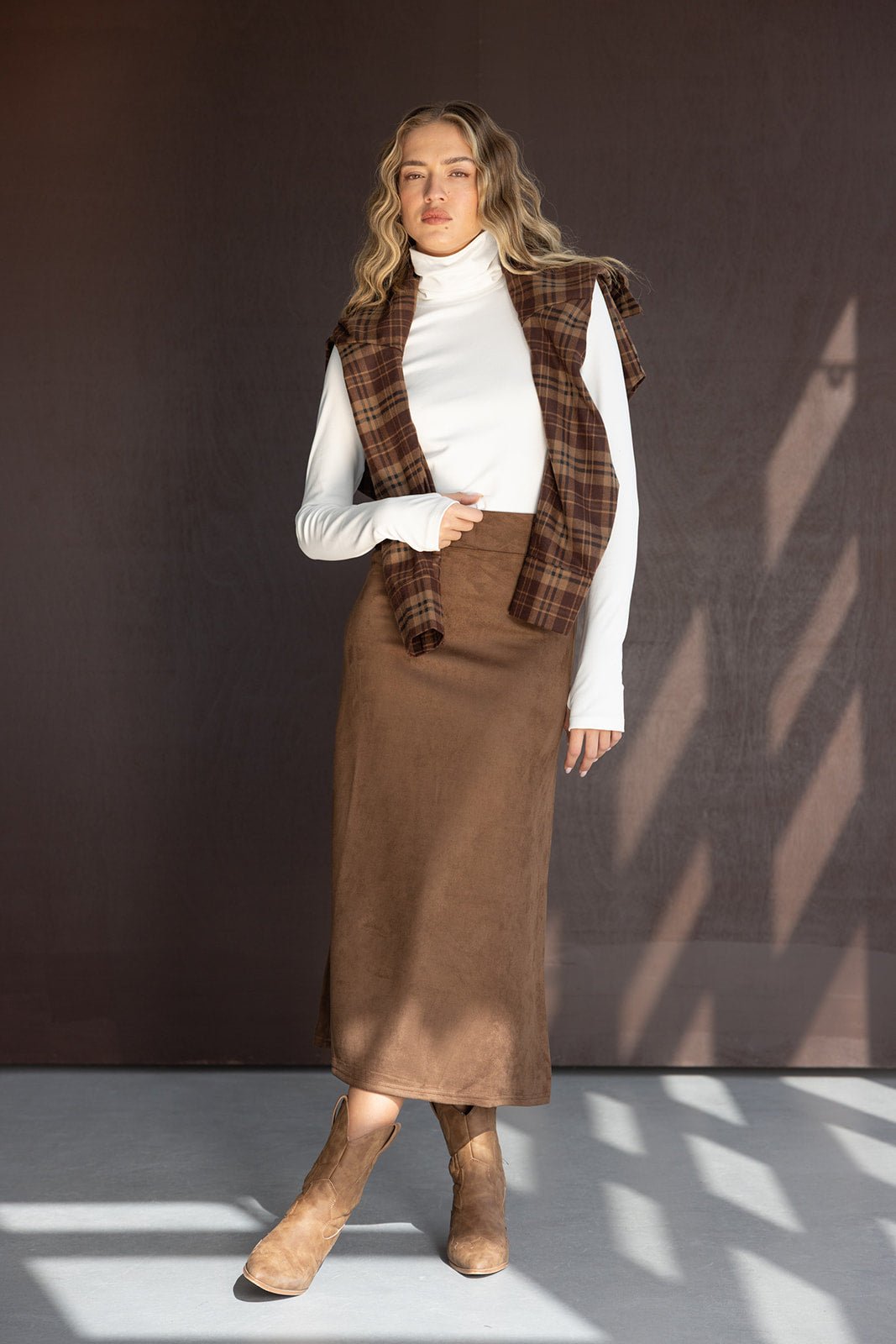 אישה עם חולצת גולף לבנה, חצאית חומה ארוכה ומגפיים חומים, בלוק קז'ואל סתיו אופנתי
