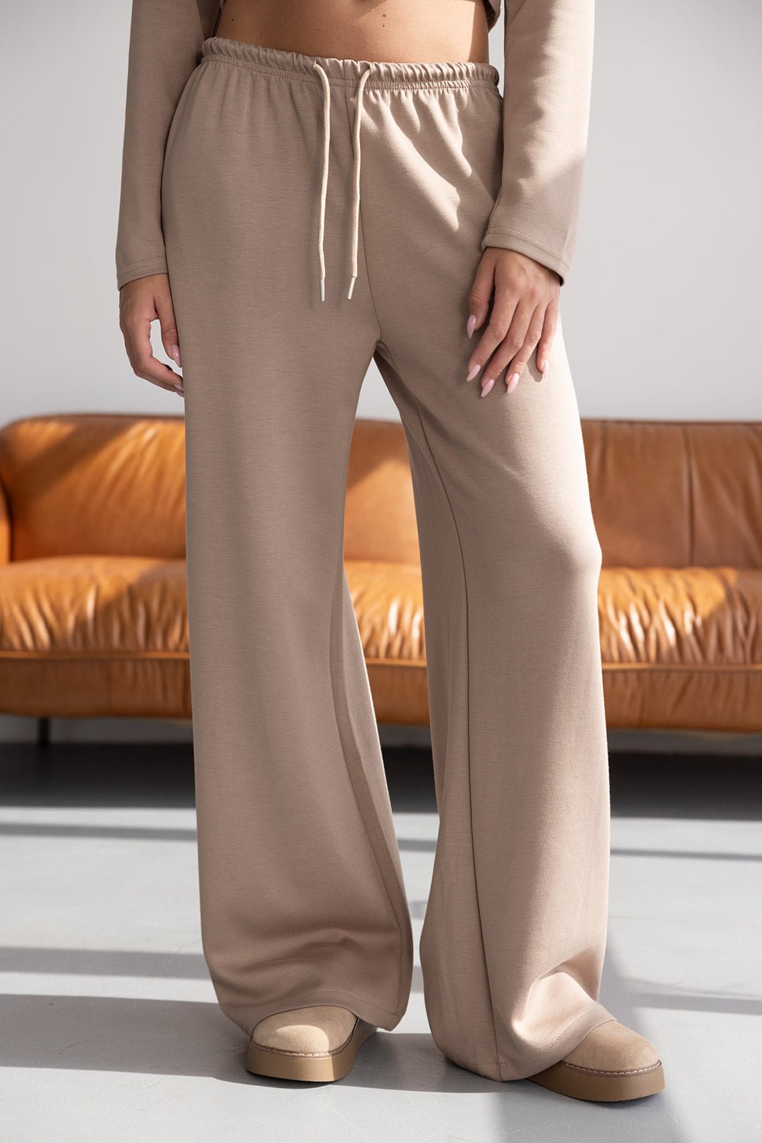 מכנסי טרנינג נשים בצבע בז', גזרה רחבה, בד רך, רקע ספה חומה