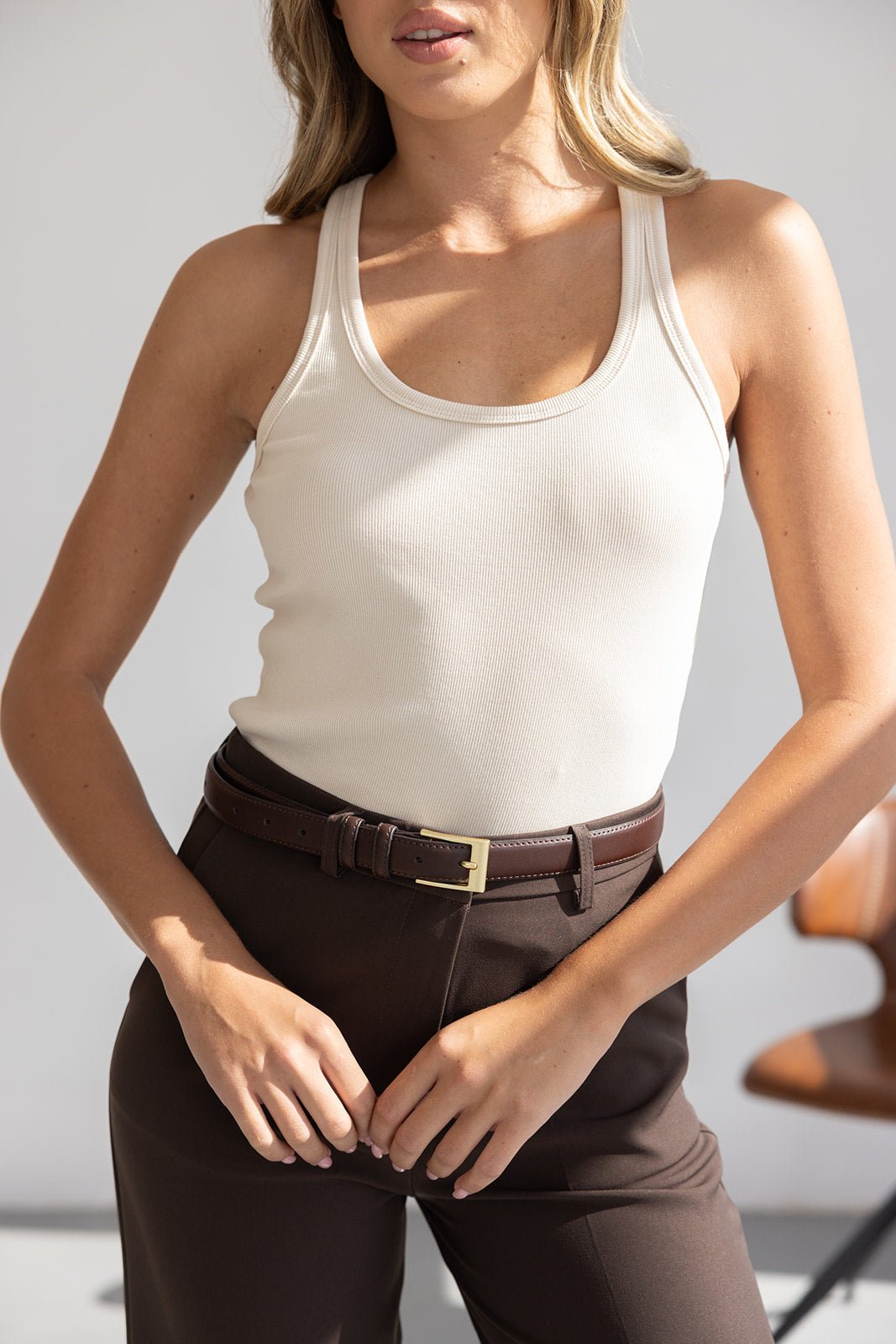 דוגמנית לובשת גופיית ריב לבנה ומכנסיים חומים עם חגורה חומה, בגדי אופנה לנשים