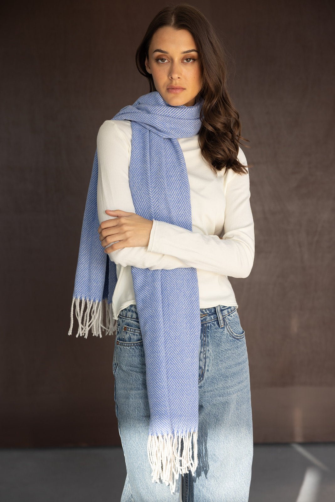 צעירה לובשת צעיף כחול עם שוליים לבנים, חולצה לבנה ומכנסי ג'ינס אופנתיים, רקע כהה