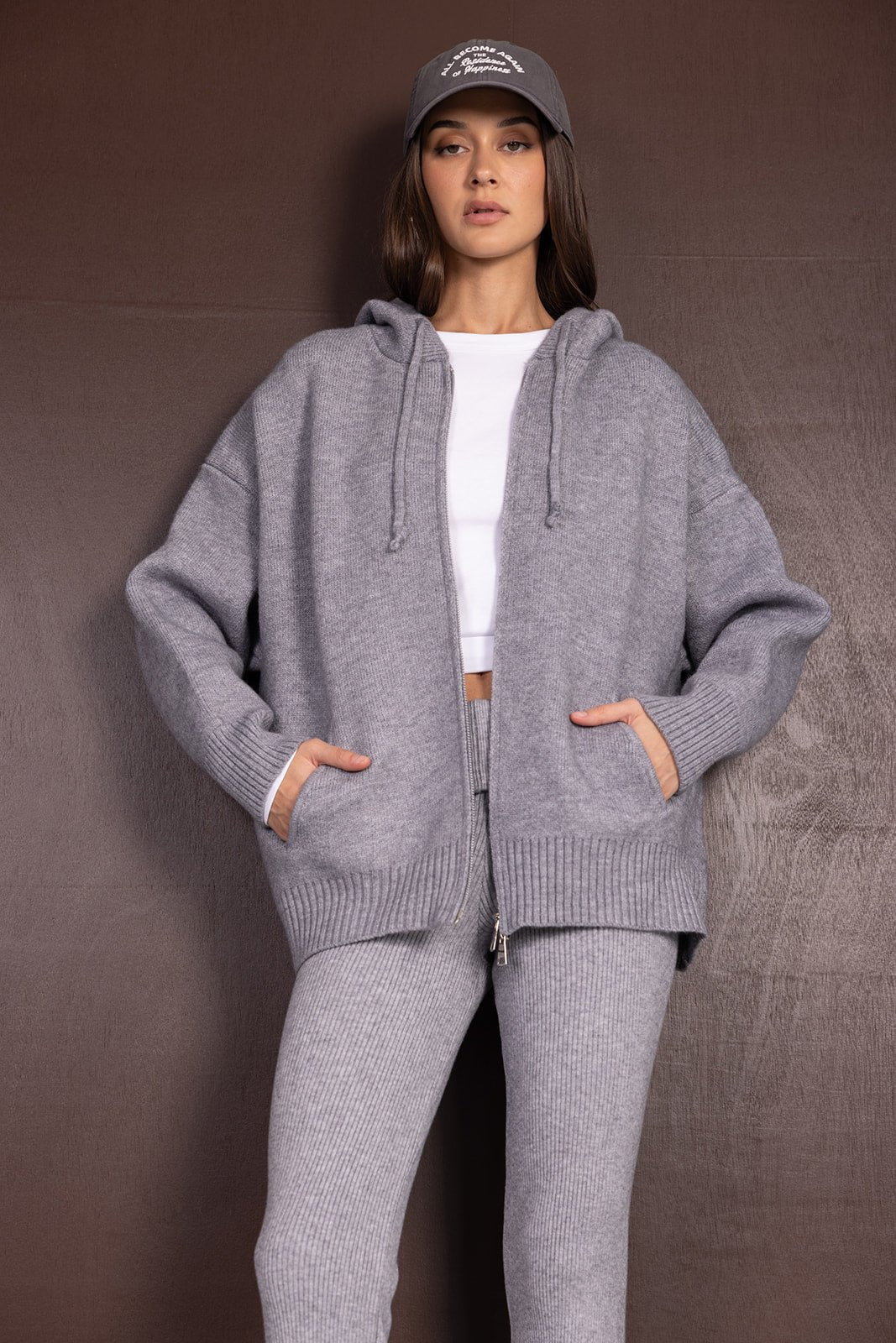 אישה לובשת סט סריג אפור שיקי, קפוצ'ון וריטון, מכנסיים תואמים וכובע אופנתי