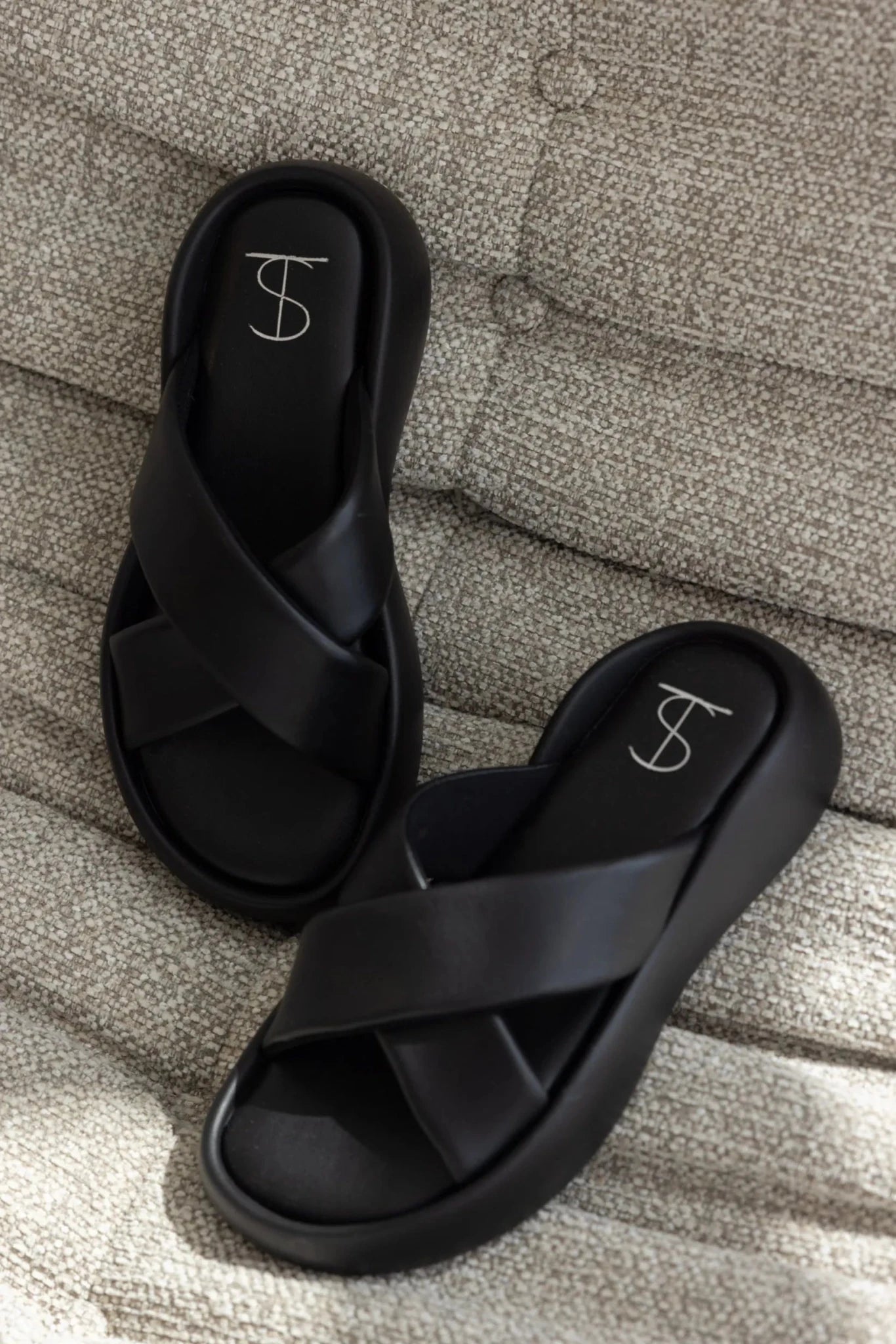 סנדלים שחורים לנשים עם רצועות מוצלבות ועיצוב מודרני מונחים על ספה בהירה