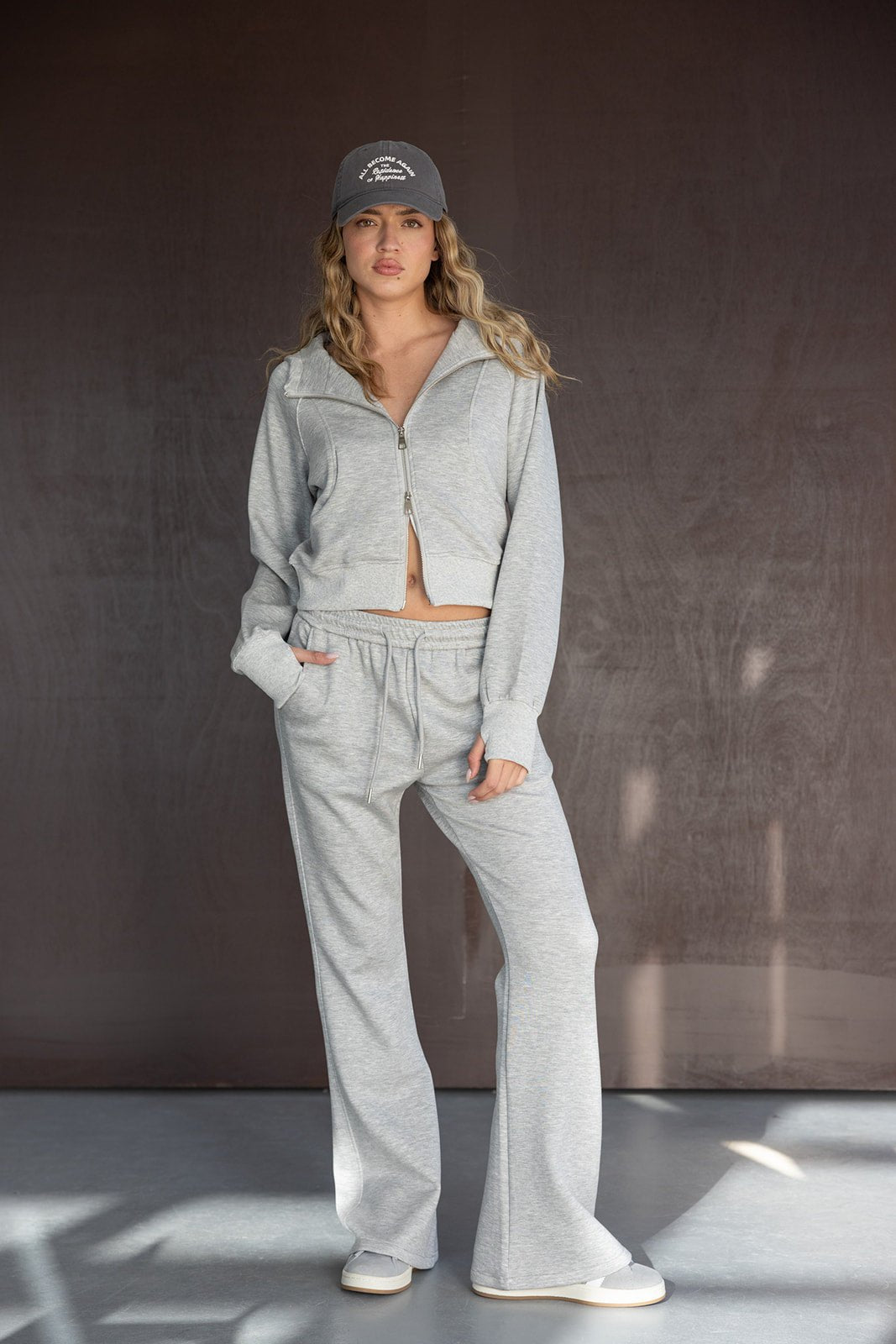דוגמנית לובשת סט טרנינג אפור עם קפוצ'ון, מכנסיים רחבים וכובע מצחייה אופנתי, על רקע כהה