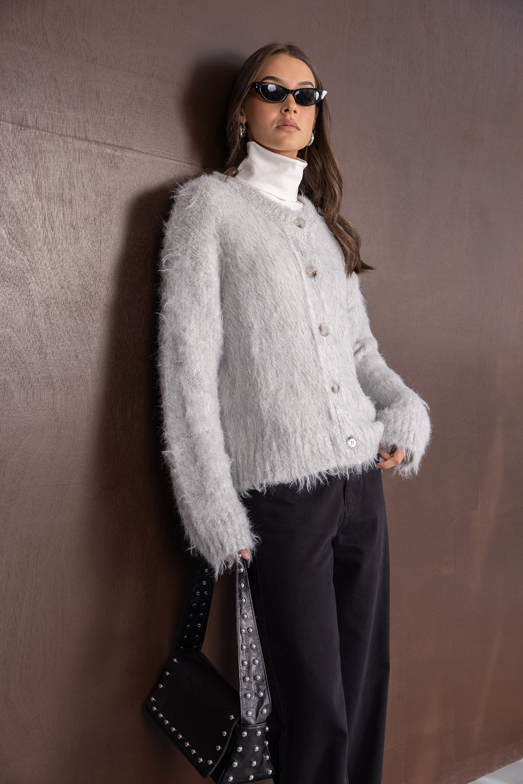 אופנת נשים: דוגמנית לובשת סוודר פרוותי אפור, מכנסיים שחורים, תיק טרנדי ומשקפי שמש