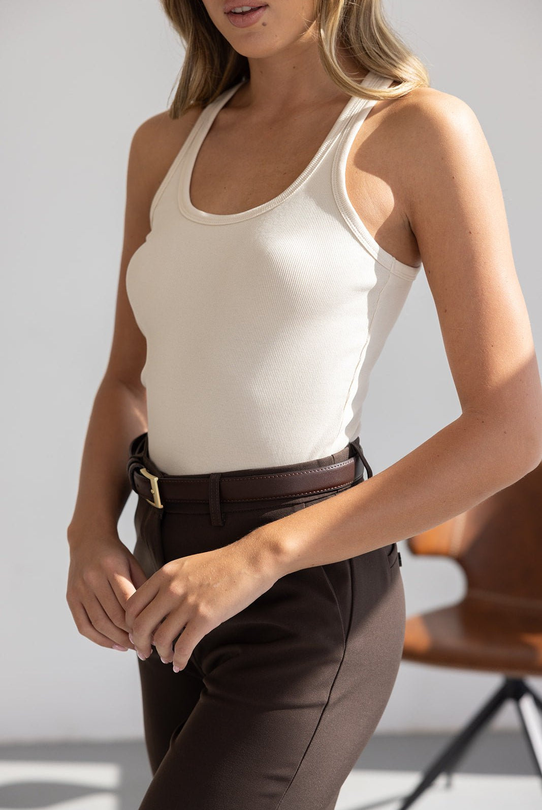 אישה לובשת גופיית סריג בז׳ ומכנסיים חומים מחויטים עם חגורה, אופנת נשים קיץ