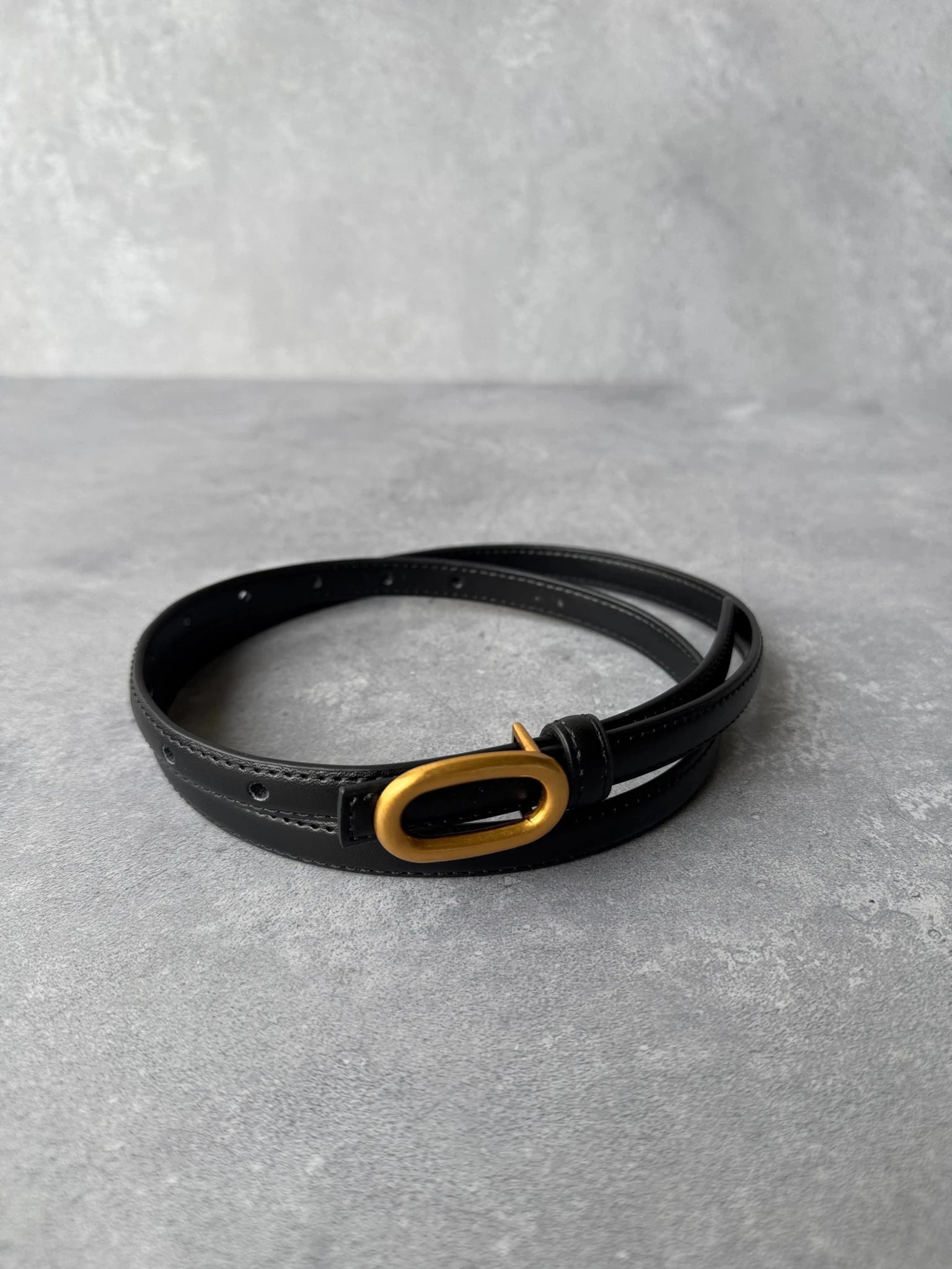 חגורת נשים שחורה עם אבזם אובלי מוזהב, צילום על רקע אפור, אקססוריז אופנתי