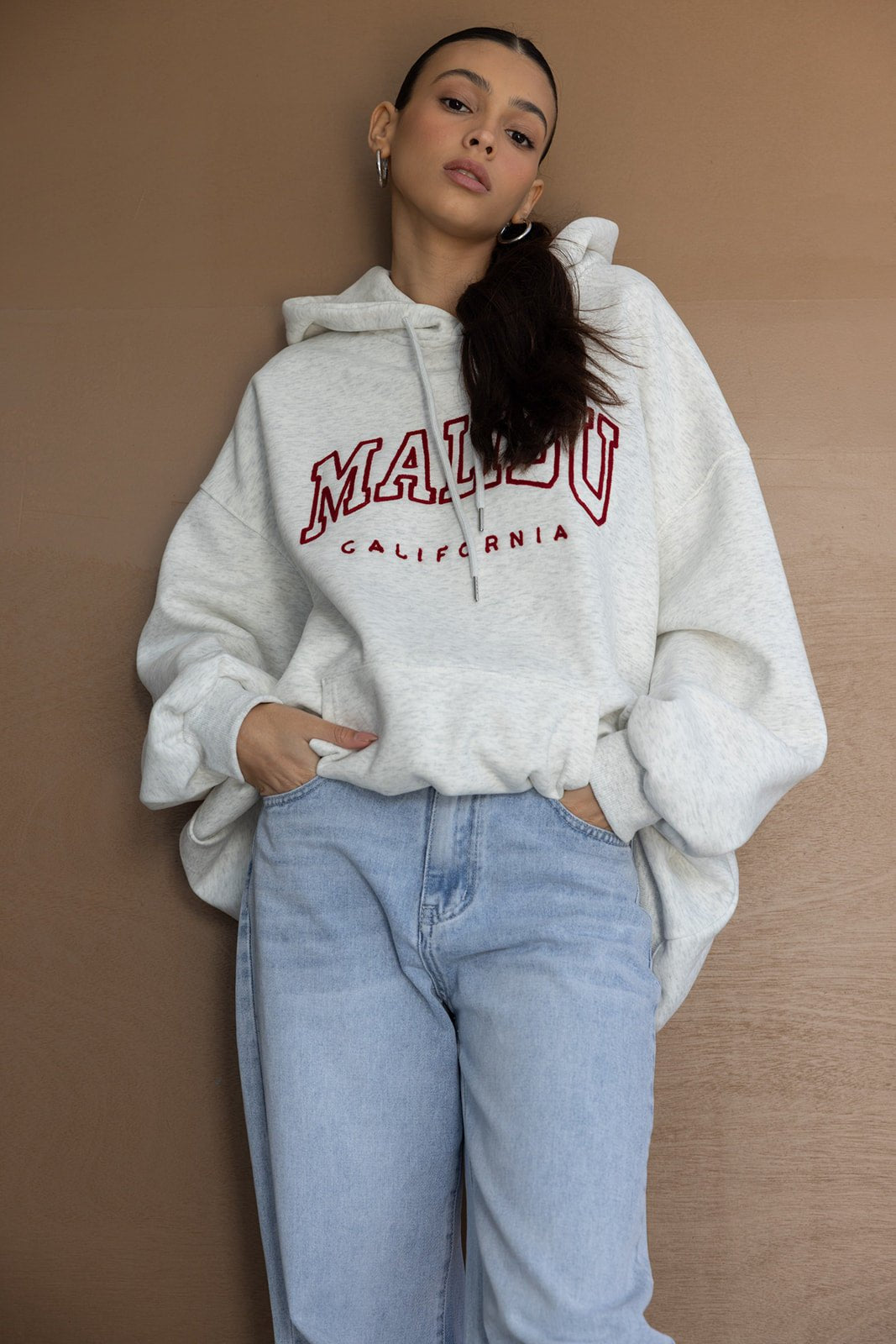דוגמנית לובשת סווטשירט אוברסייז אפור עם כיתוב MALIBU וג'ינס בגזרה גבוהה, אופנת נשים צעירה ובסגנון קז'ואל