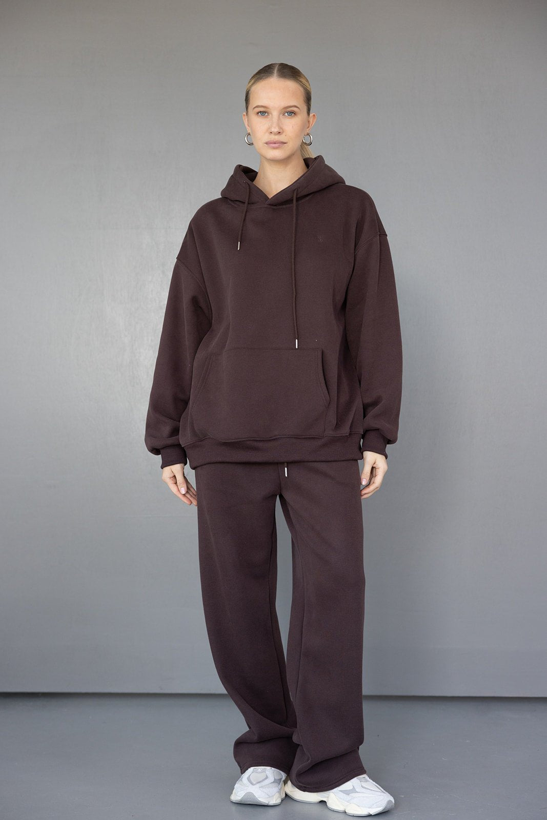 אישה לובשת סט קז'ואל חורפי בגוון חום שוקולד, הכולל קפוצ'ון ומכנסיים רחבים, נעלי סניקרס אופנתיות