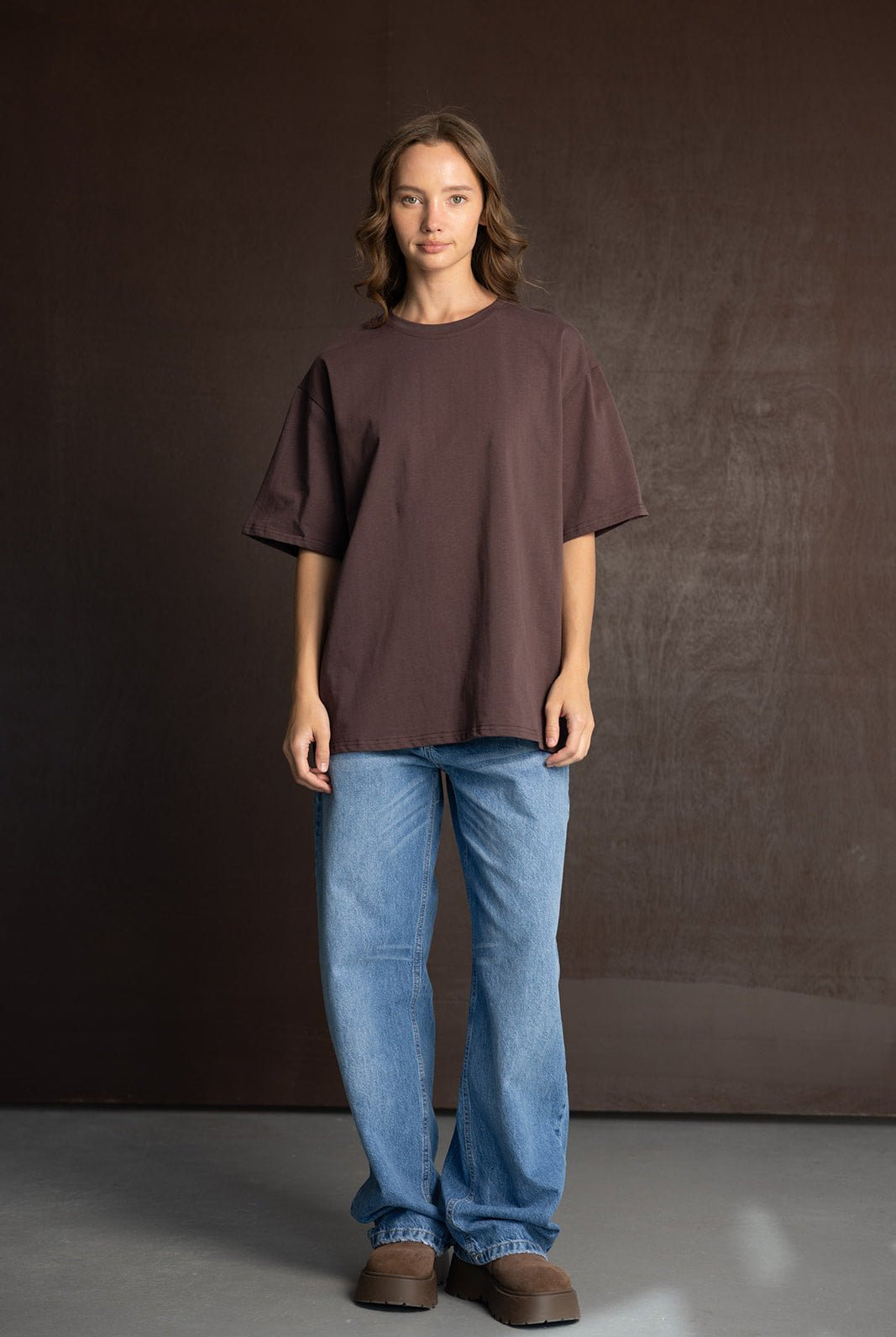 אישה לובשת טי שירט חומה רחבה ומכנסי ג'ינס בגזרה רחבה, סטייל קז'ואל אופנתי לנשים