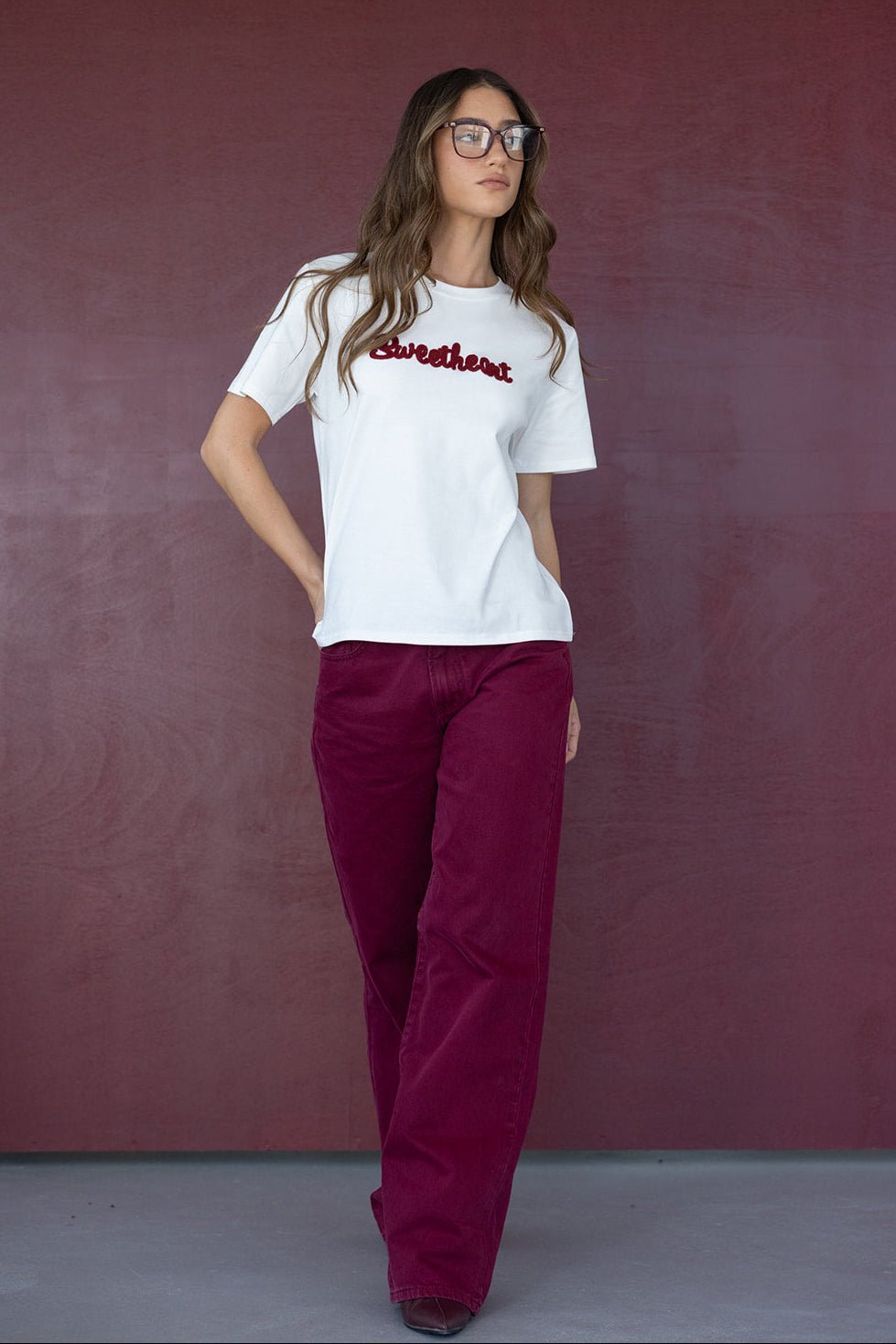 אישה עם חולצת טי שיירט לבנה עם כיתוב אדום ומכנסיים בורדו רחבים, אופנת נשים צעירה וטרנדית