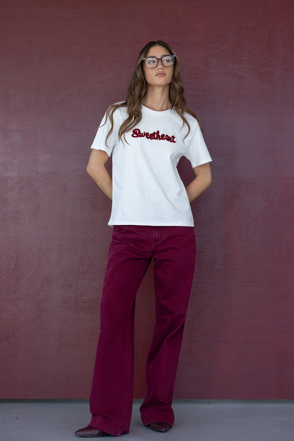 אישה לובשת חולצה לבנה עם הכיתוב Sweetheart ומכנסיים בורדו, אופנת קז'ואל לנשים