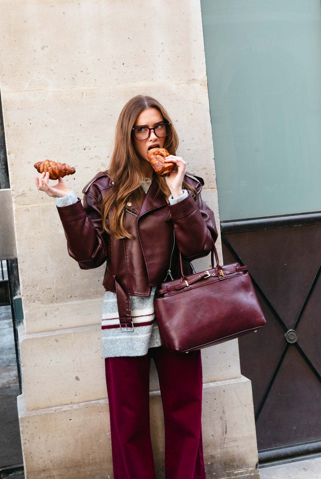 אישה אופנתית עם מעיל בורדו ותיק תואם, אוכלת קורסון ברחוב עירוני