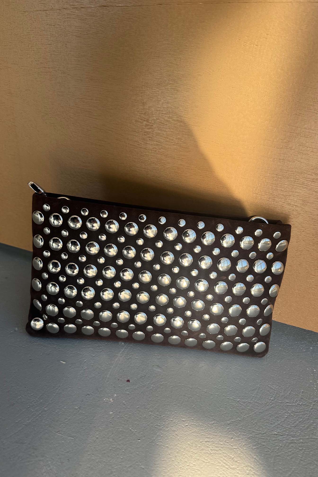 קלאץ' אופנתי לנשים בצבע שחור עם ניטים כסופים, תיק ערב מעוצב מונח על רקע בהיר