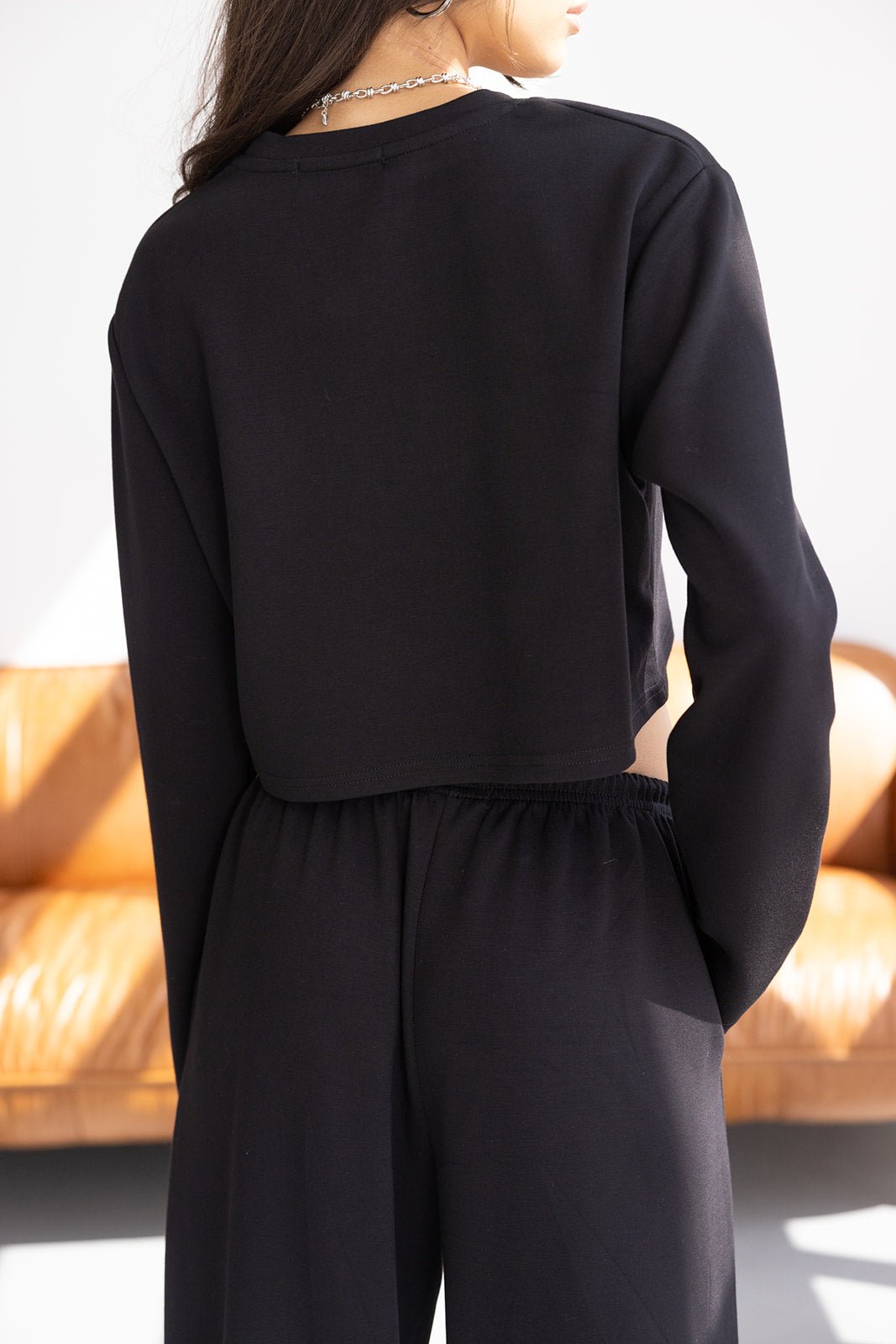 אישה עם שיער ארוך לובשת סט טרנינג שחור מבד רך, חולצה ארוכה ומכנסיים, צילום מאחור