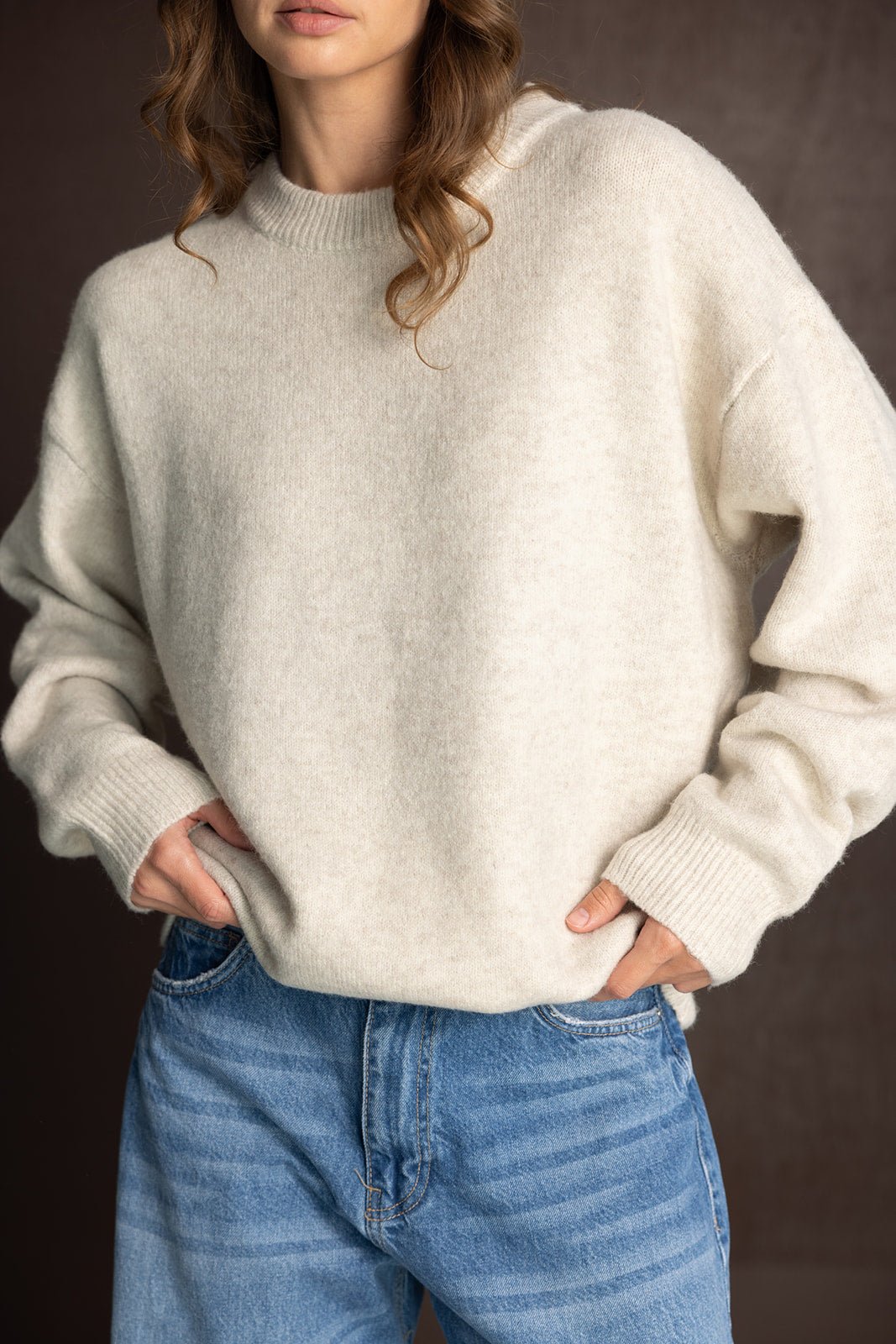 אישה לובשת סוודר צמר לבן ומכנסי ג'ינס אופנתיים, בגדי חורף לנשים