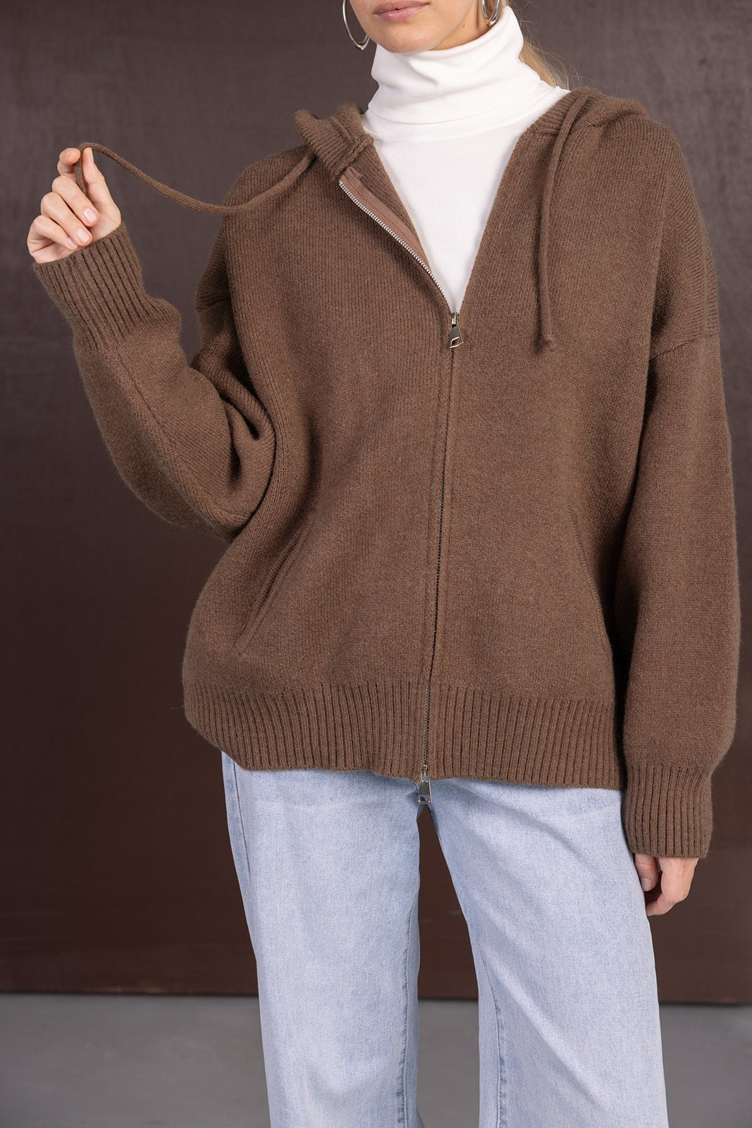 אישה לובשת סוודר חום עם רוכסן וקפוצ'ון, ג'ינס בהיר וגולף לבן, אופנת חורף לנשים