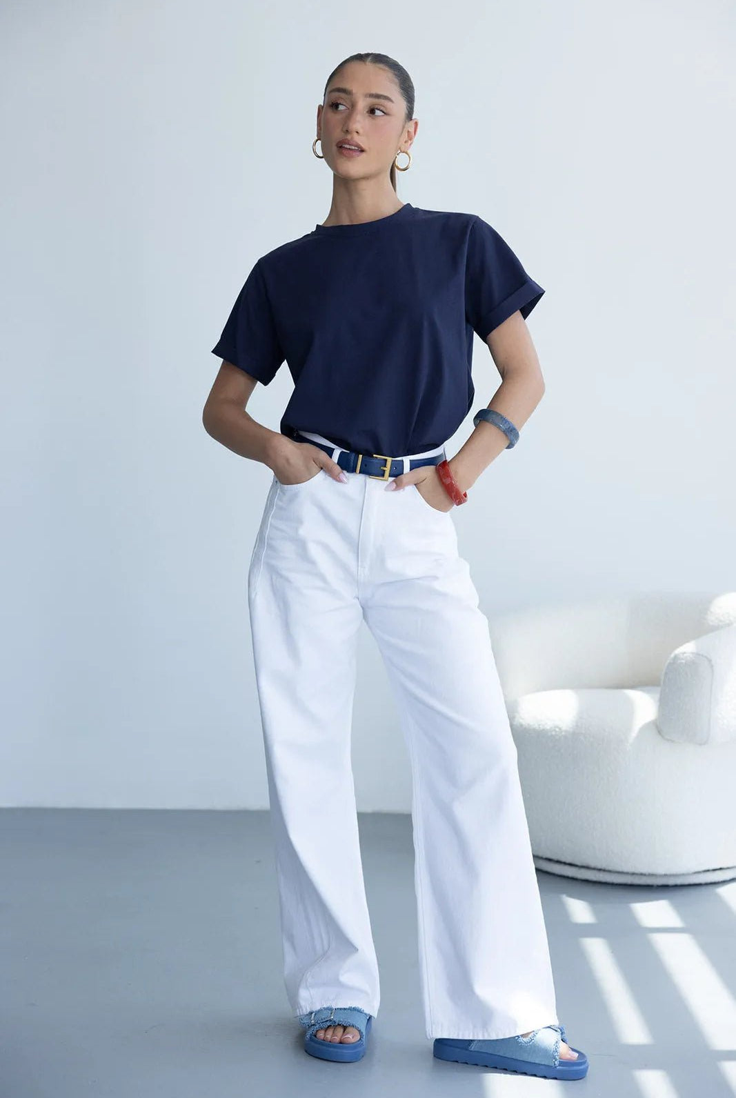 אישה לובשת טי-שירט כחולה, מכנסי ג'ינס לבנים רחבים וסנדלים כחולים, מראה אופנתי קז'ואל לנשים