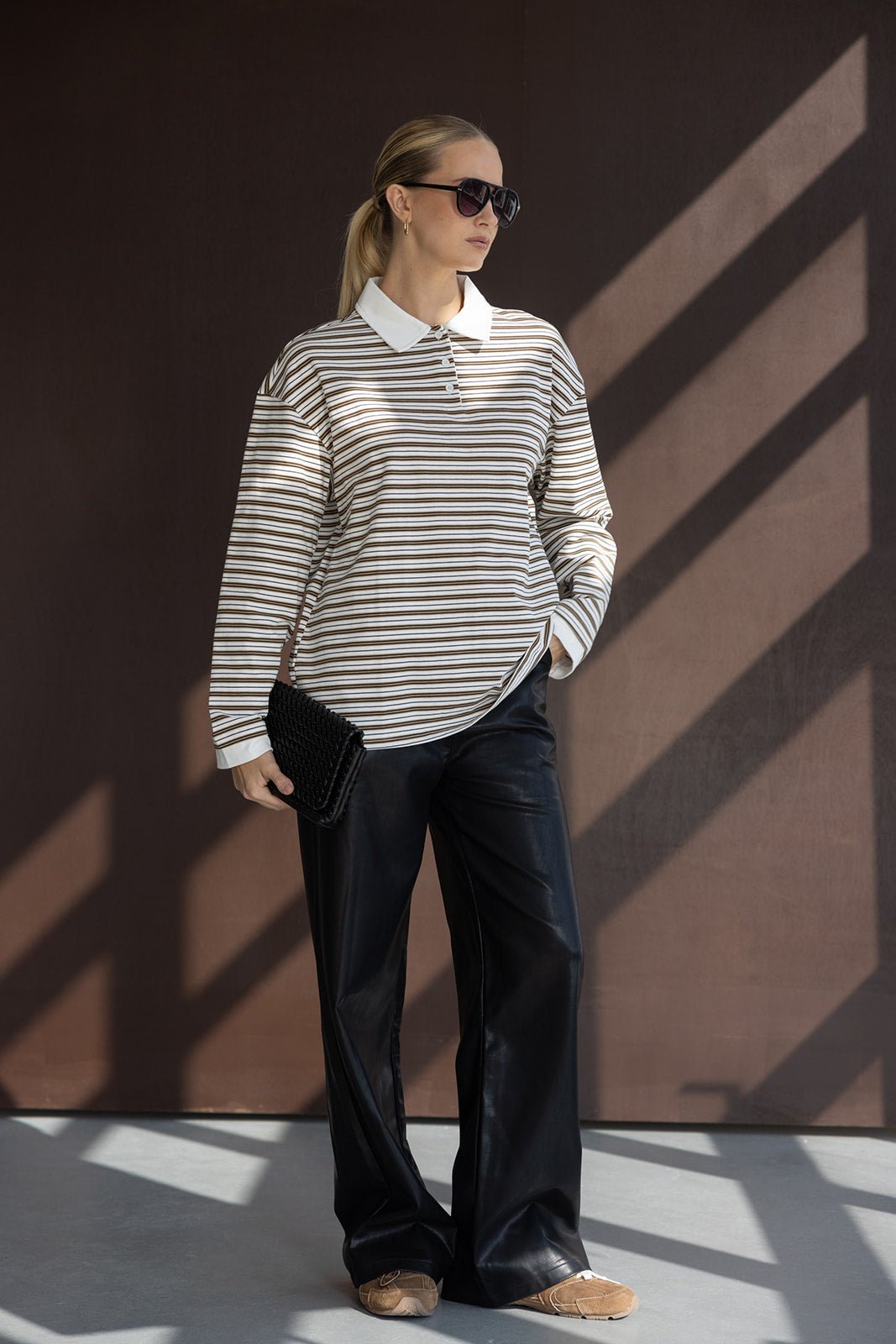אישה לובשת חולצת פסים עם צווארון לבן, מכנסי עור שחורים, משקפי שמש ותיק קלאץ', אופנה לנשים