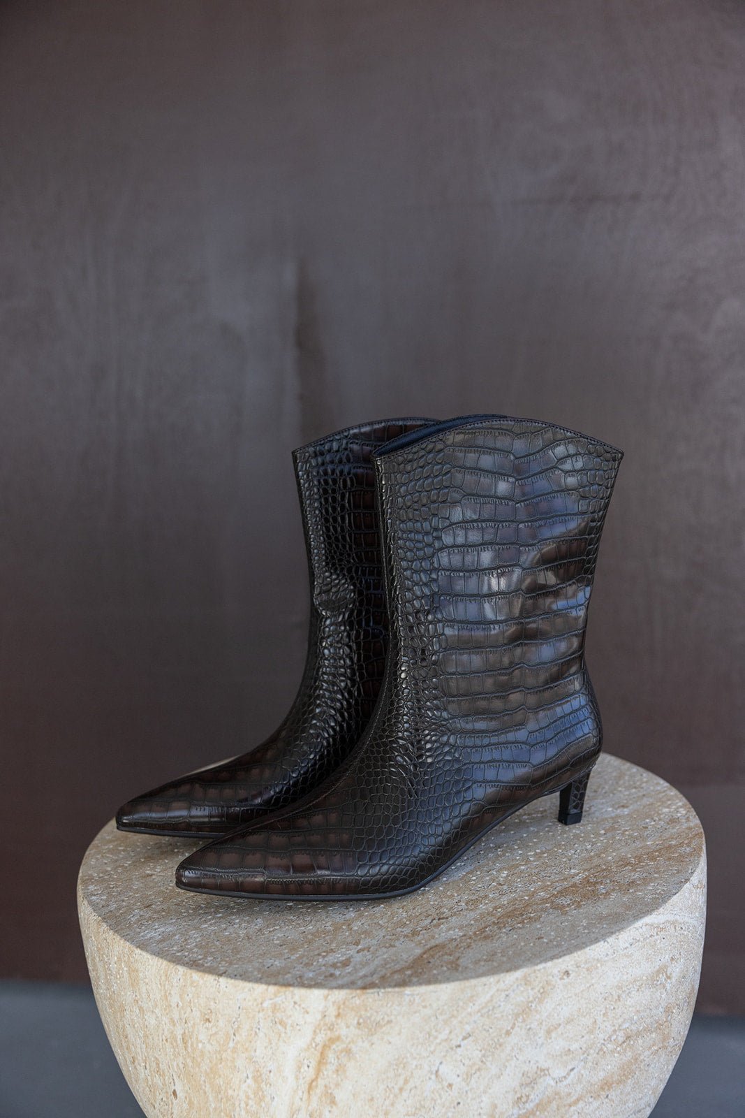 מגפי נשים חומים עם טקסטורת עור קרוקודיל, עקב נמוך, מונחים על שולחן אבן