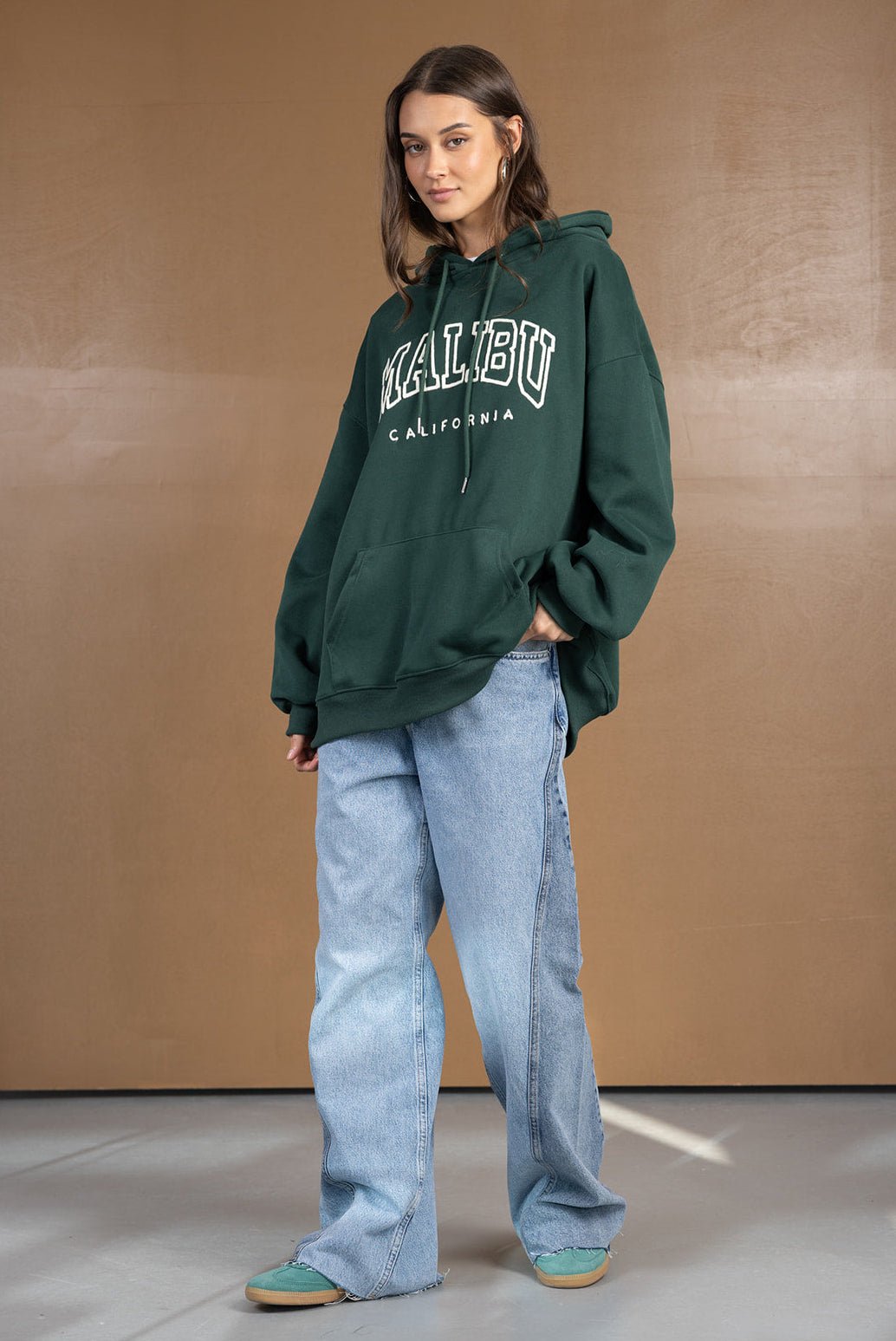 דוגמנית בלבוש קז'ואל אופנתי לובשת קפוצ׳ון ירוק MALIBU קליפורניה וג׳ינס רחב, אופנת רחוב לנשים