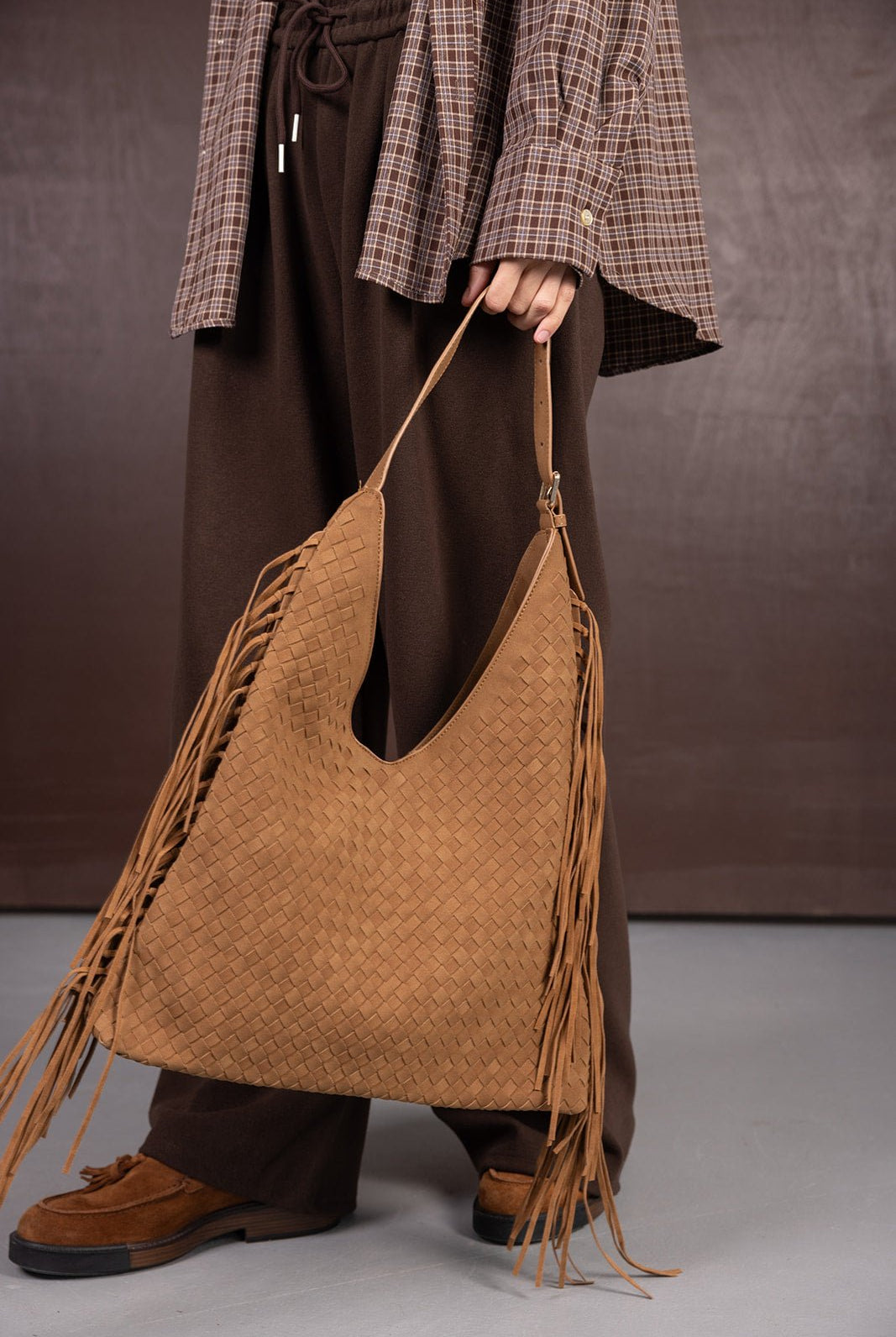 תיק חום קלוע עם פרנזים, משולב עם מכנסיים חומים וחולצה משובצת אופנתית לנשים