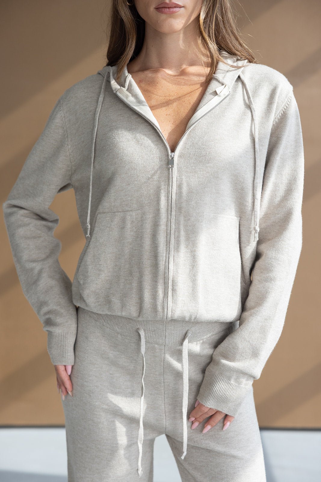 אישה לובשת סט בגדי פנאי אפור בהיר לנשים, קפוצ'ון רוכסן ומכנסיים מחממים, אופנתיות לנערות