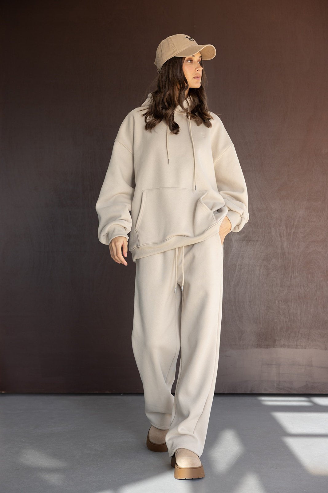 אישה לובשת סט קפוצ׳ון ומכנסיים בגוון בז׳, כובע מצחייה ונעליים תואמות, אופנת נשים עדכנית