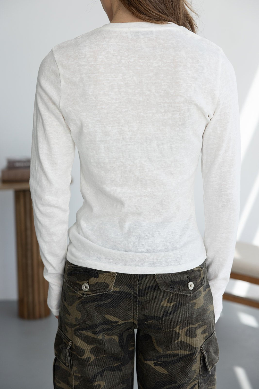 אישה בלבוש אופנתי עם חולצת בד לבנה ארוכה ומכנסי דמוי קאמופלאז' ירוקים, צילום מאחור